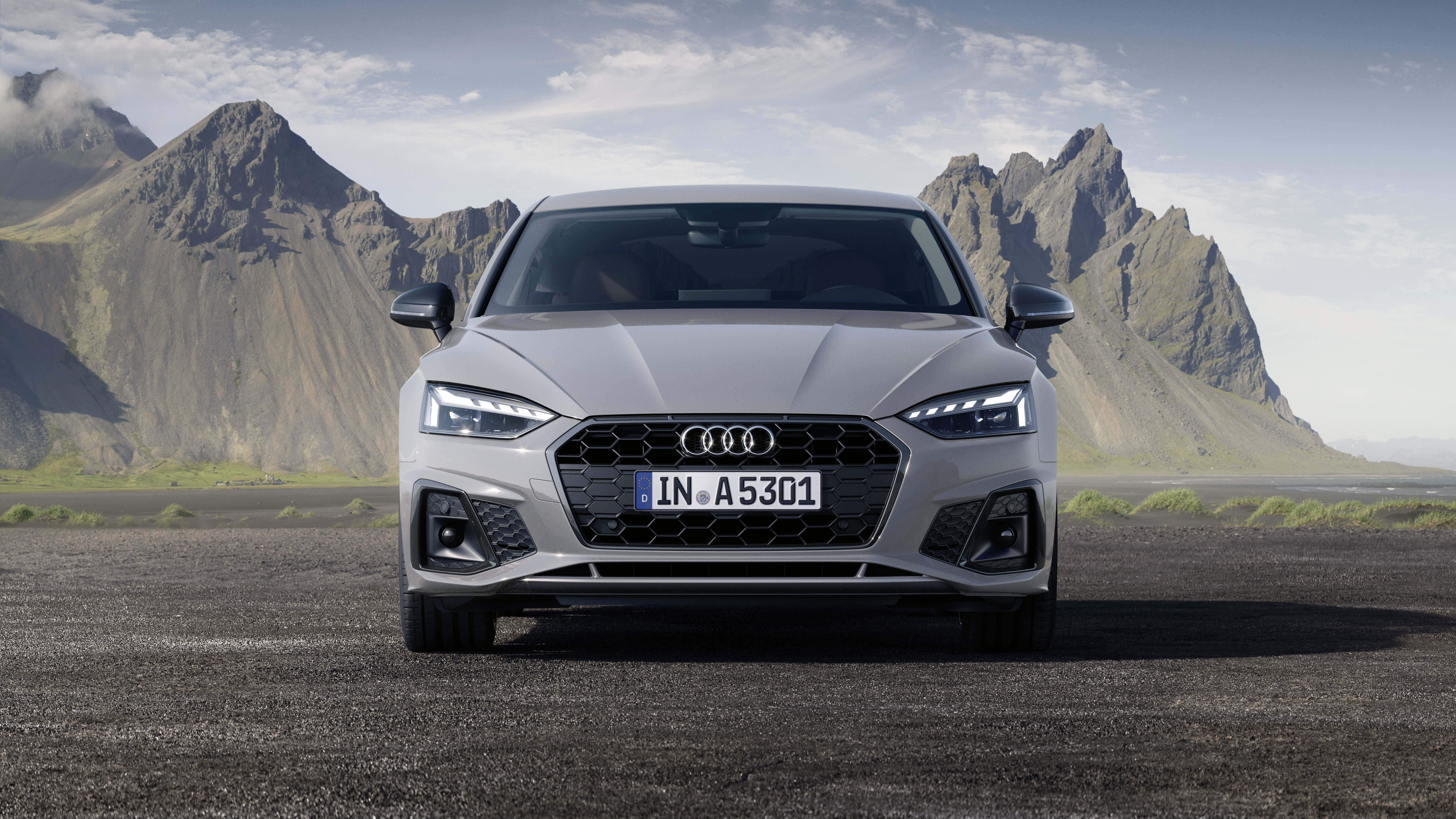 Audi A5 桌布 壁紙 — 一部時尚的銀色奧迪A5跑車在碎石平原上向前行駛，背後是鋸齒狀的火山山脈，天空局部多雲。