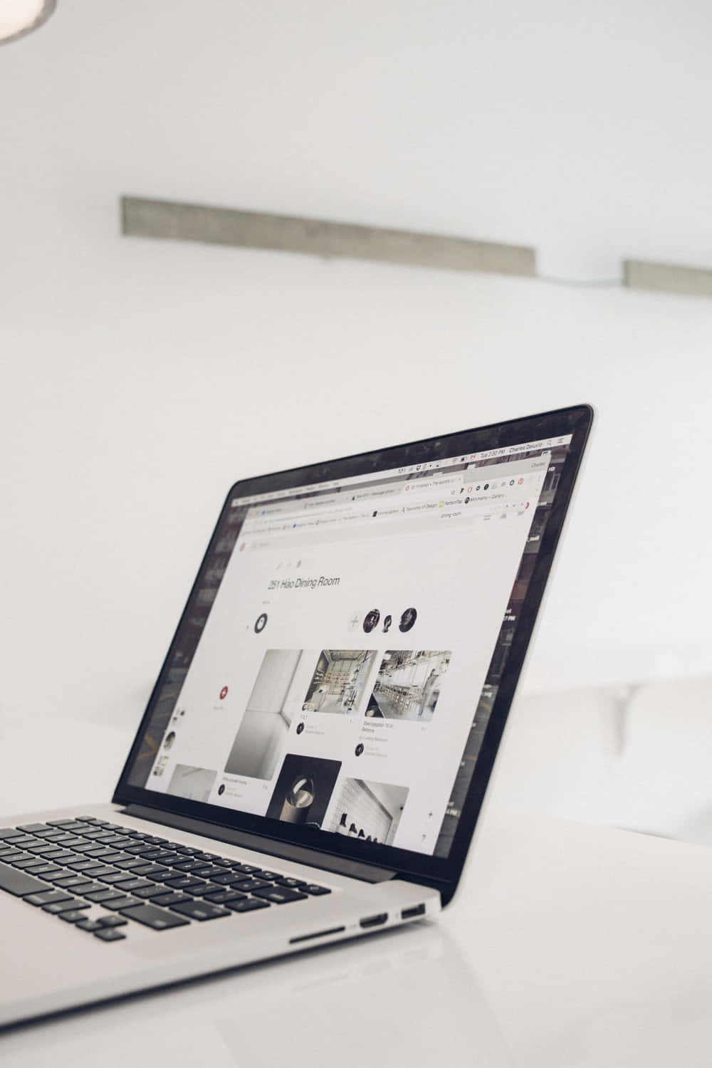 Website 桌布 壁紙 — 一部時尚的銀色手提電腦在柔和的自然光下，於明亮的白色桌子上顯示一個極簡主義的室內設計網站。