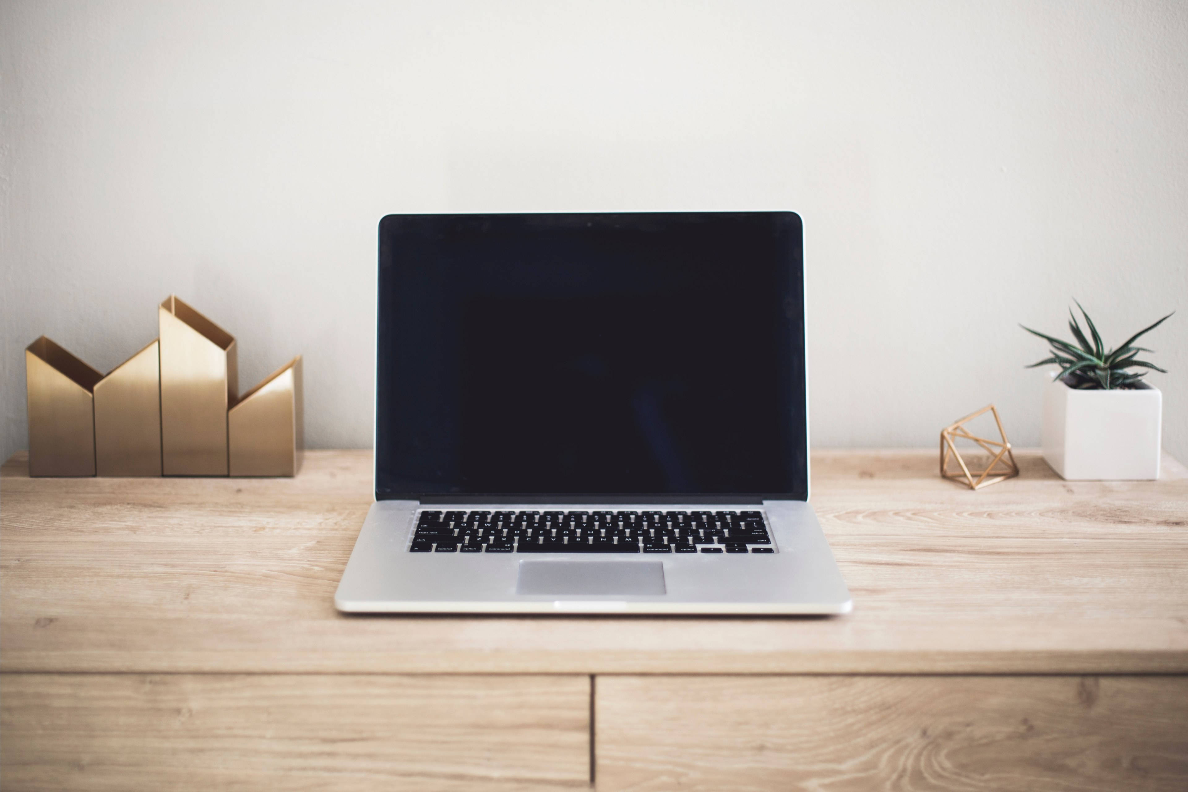 Laptop 桌布 壁紙 — 一部時尚的銀色手提電腦放在淺色木桌中央，兩側擺放金色幾何裝飾和一個小盆栽多肉植物。