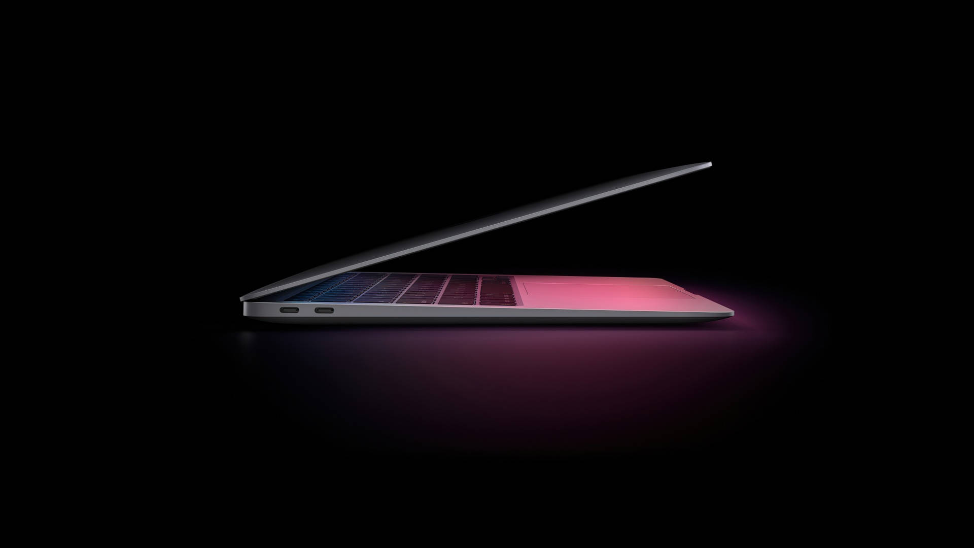 macOS Mojave MacBook Air 壁紙 — 一部時尚的銀色筆記型電腦斜開在黑色背景上，鍵盤和觸控板散發出粉紅色和藍色的光芒。