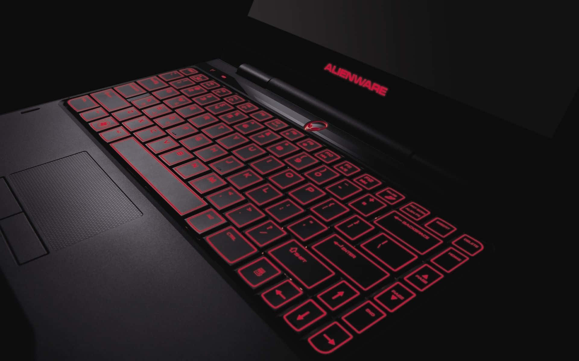 Best Laptop 桌布 壁紙 — 一部時尚的黑色Alienware筆記型電腦，在黑暗背景下帶有發光的紅色背光按鍵和標誌。