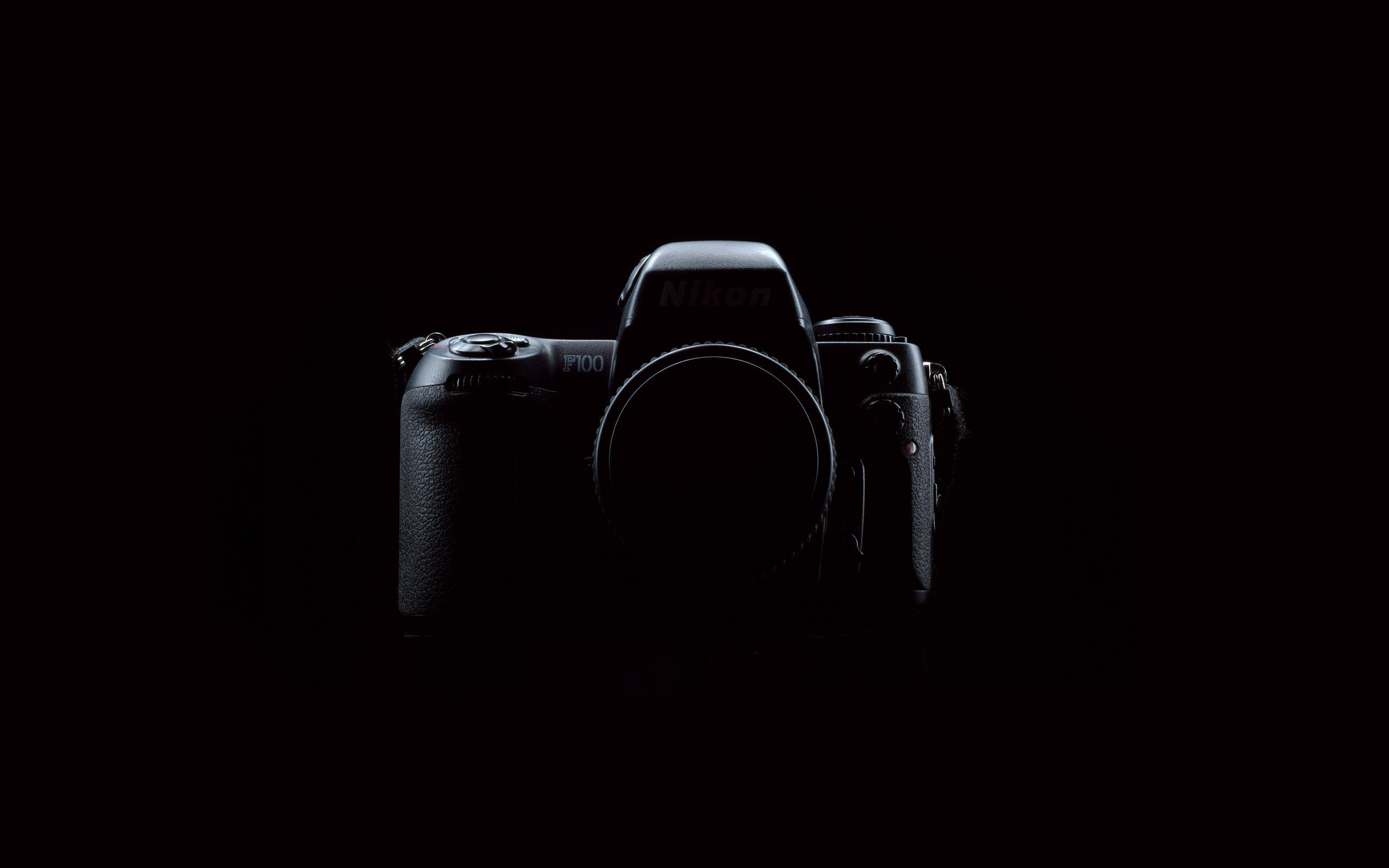  壁紙 — 一部時尚的黑色Nikon F100相機機身，在漆黑背景中微微發光。