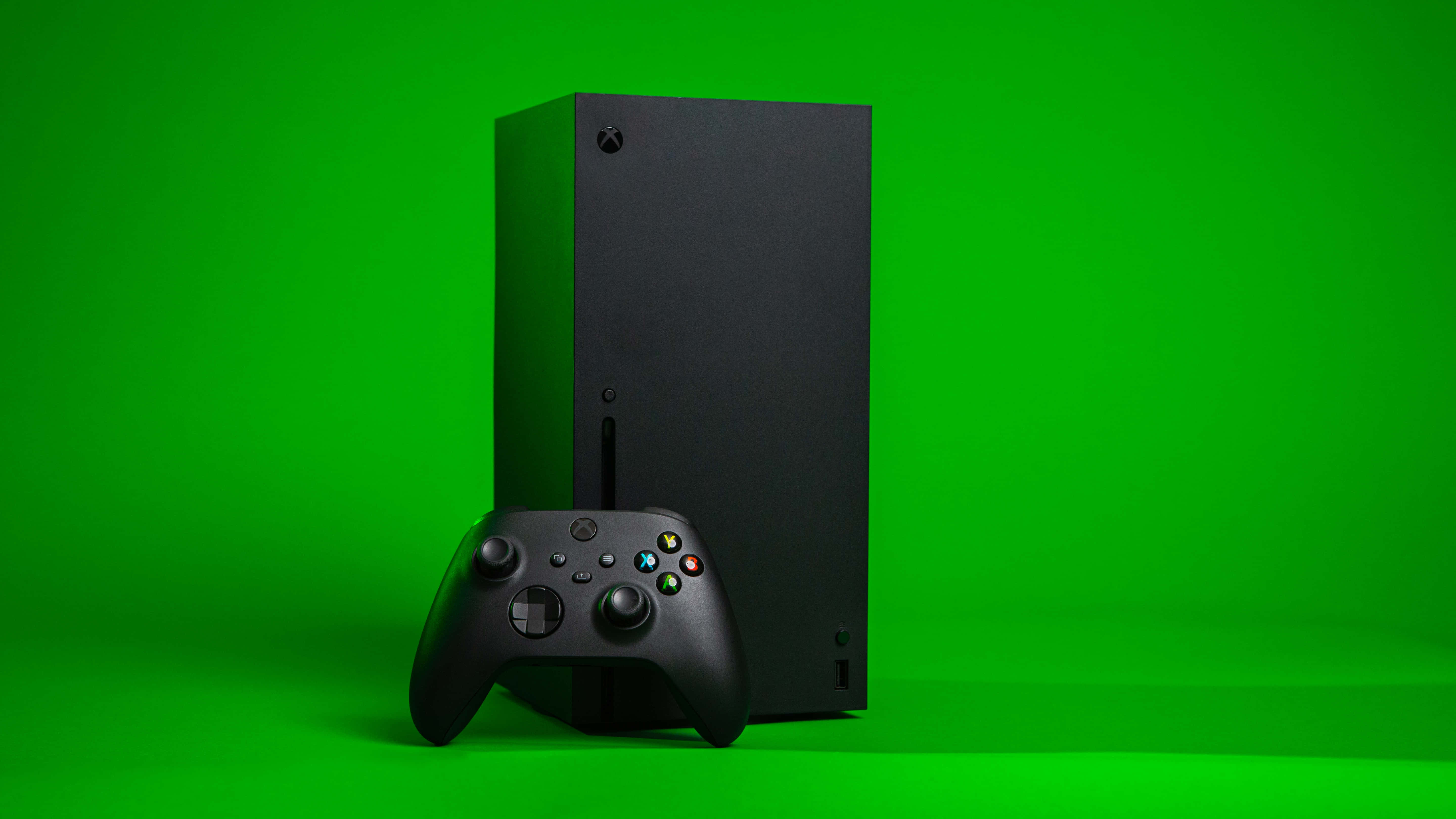 Gaming Consoles 桌布 壁紙 — 一部時尚的黑色Xbox Series X主機和控制器，在充滿活力的綠色工作室背景前矗立。