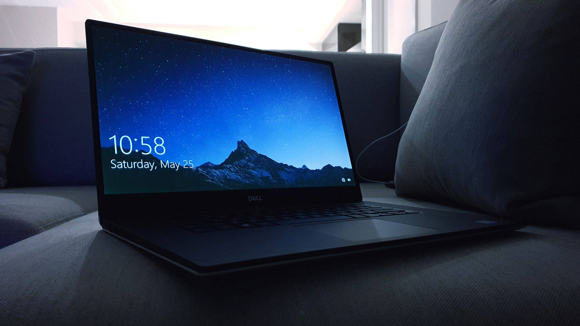 Laptop 桌布 壁紙 — 一部時尚的黑色手提電腦放在灰色梳化上，顯示一幅有雪山的星空夜間桌布。