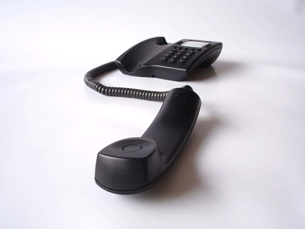 Phone Call 桌布 壁紙 — 一部時尚的黑色有線電話，帶有螺旋線，放在純白表面上，投下柔和陰影。