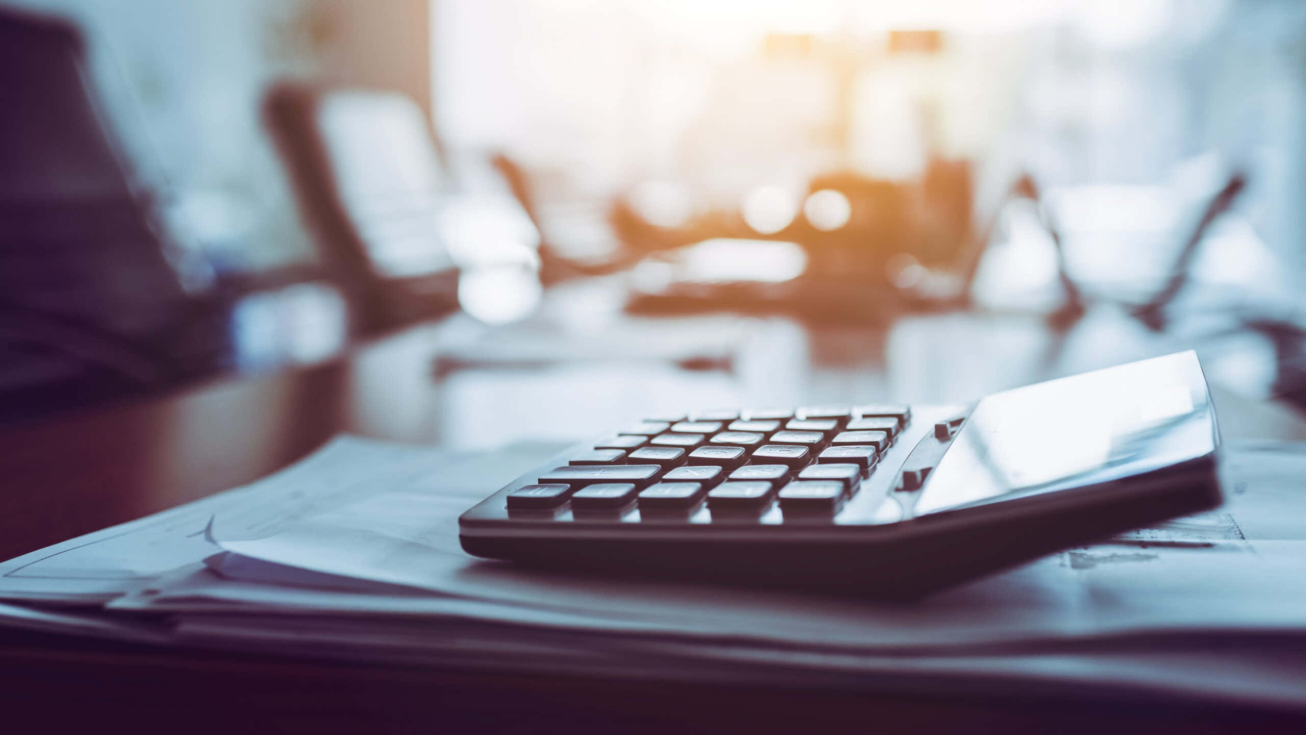 Calculator 桌布 壁紙 — 一部時尚的黑色計算器放在木桌的財務文件上，溫暖的陽光透過模糊的辦公室窗戶照射進來。
