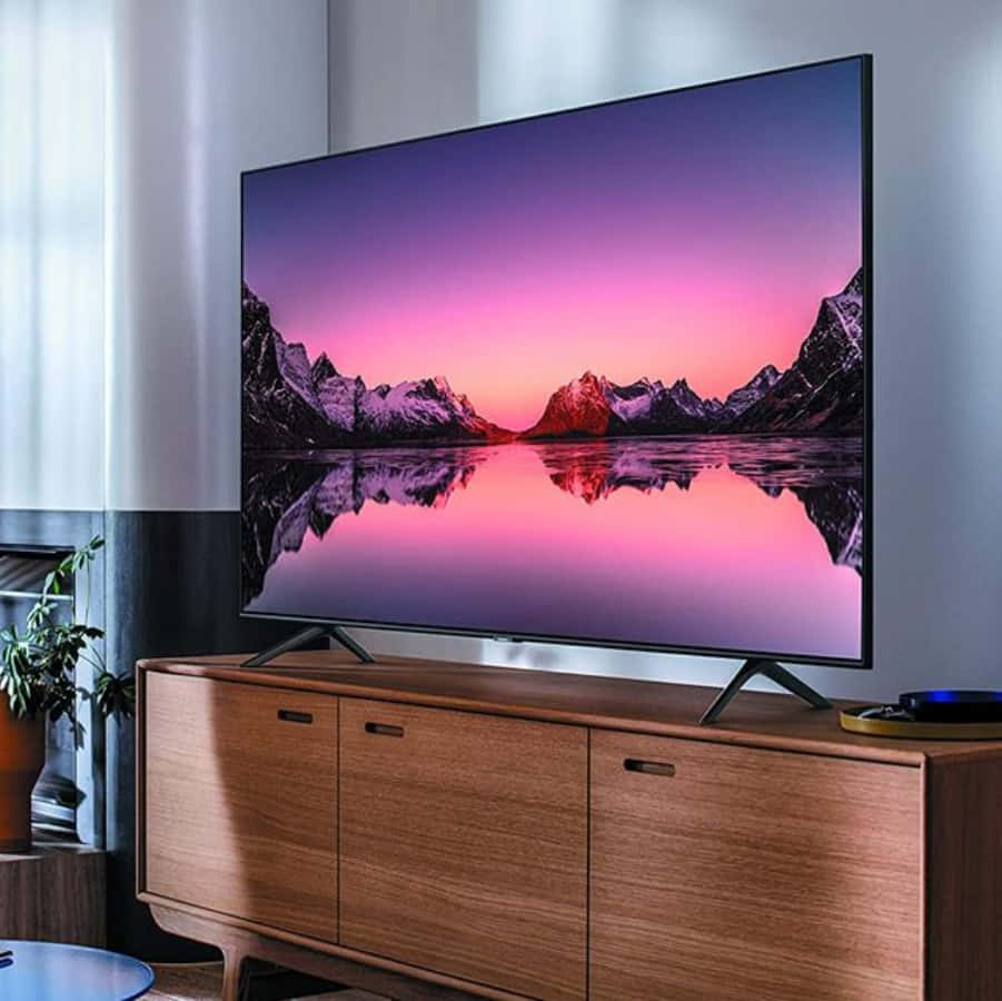 tv 桌布 壁紙 — 一部時尚電視顯示出日落時分壯麗的山湖景色，鮮豔的粉紅色和紫色色調完美地倒映在平靜的水面上。