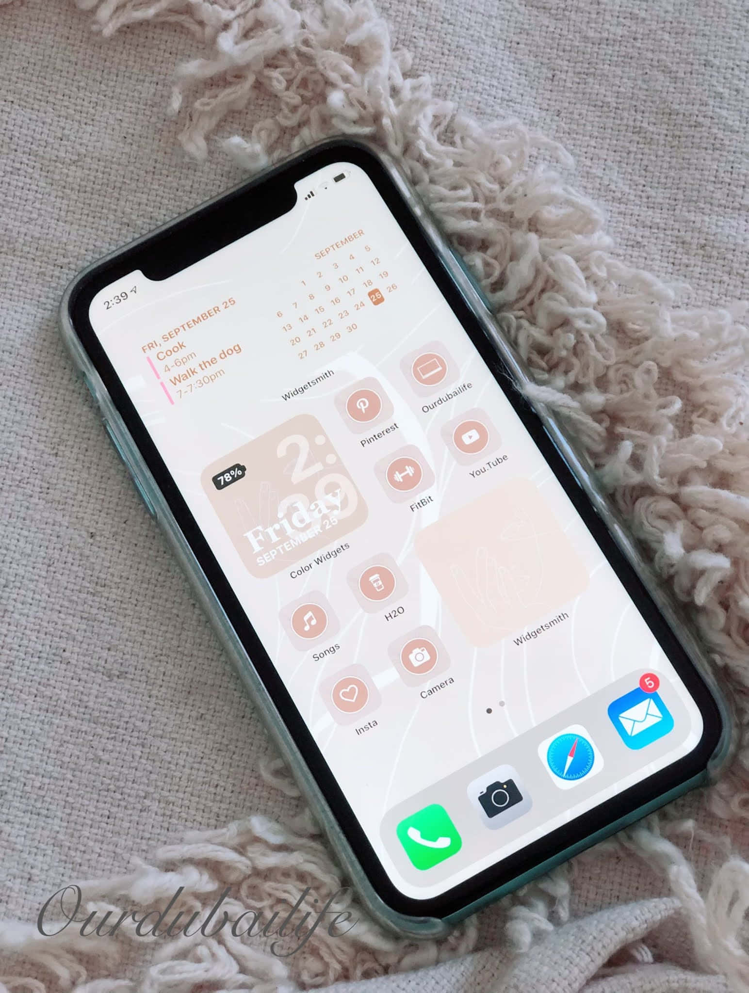 iPhone風格壁紙 桌布 壁紙 — 一部智能手機，其主屏幕為粉彩粉紅和蜜桃色，充滿小工具，放在柔軟的質感米色毯子上。
