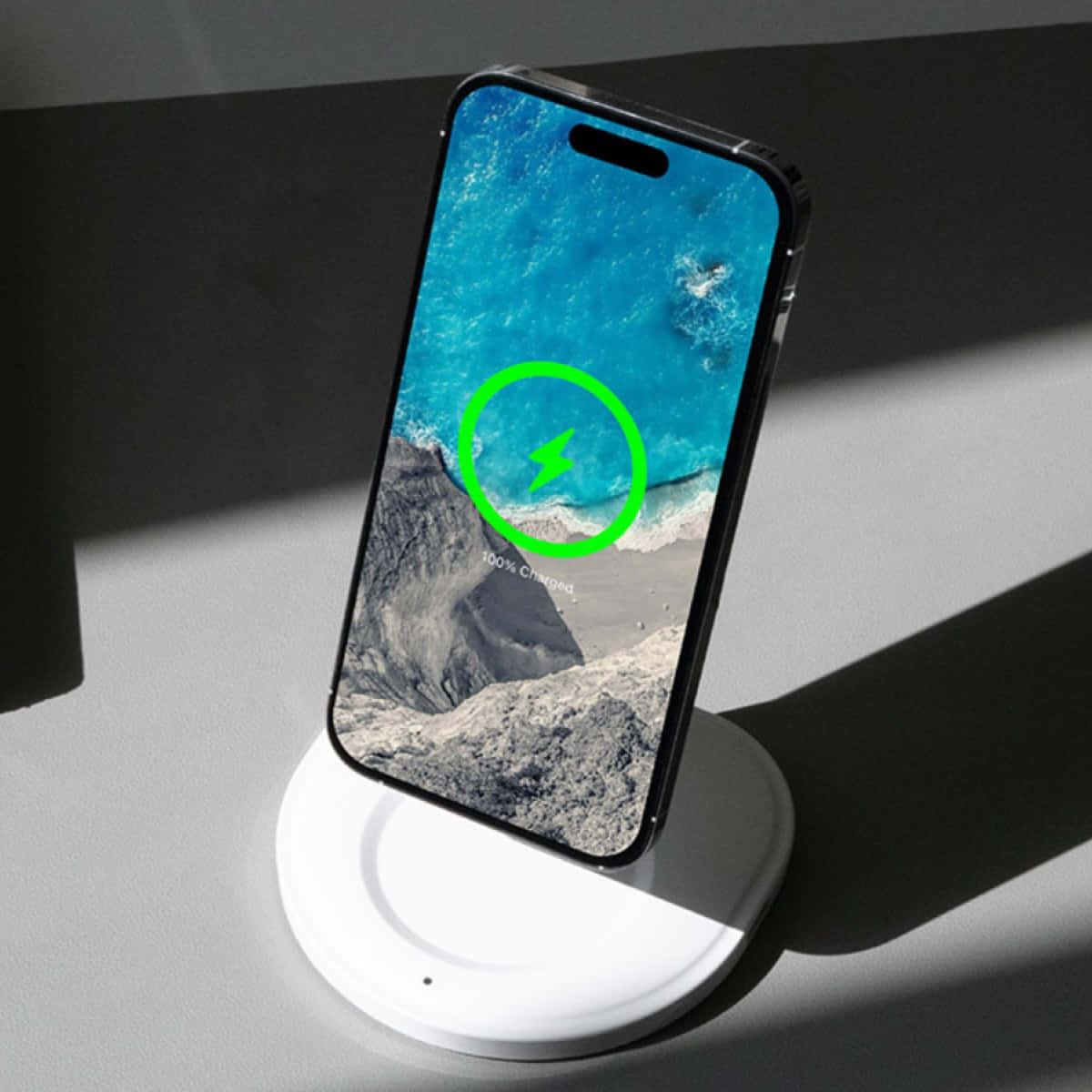 Wireless Charging 桌布 壁紙 — 一部智能手機在白色無線充電器上顯示充滿活力的海洋壁紙，帶有綠色充電圖標和「100% 已充電」文字。