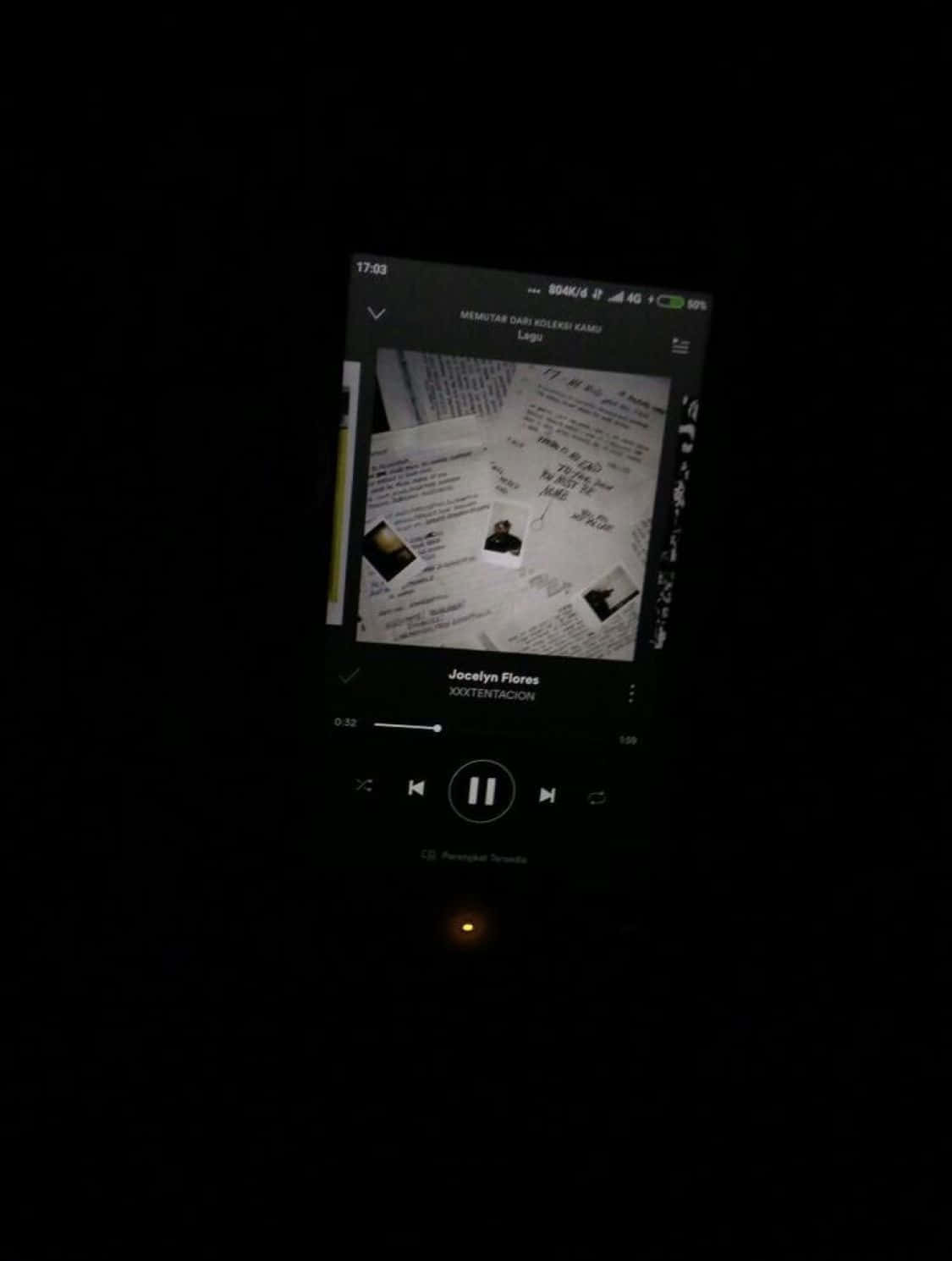 Aesthetic Grunge Phone 桌布 壁紙 — 一部智能手機屏幕在黑暗中發光，顯示一個音樂播放器，帶有黑白專輯封面，上面散佈著手寫筆記和照片。
