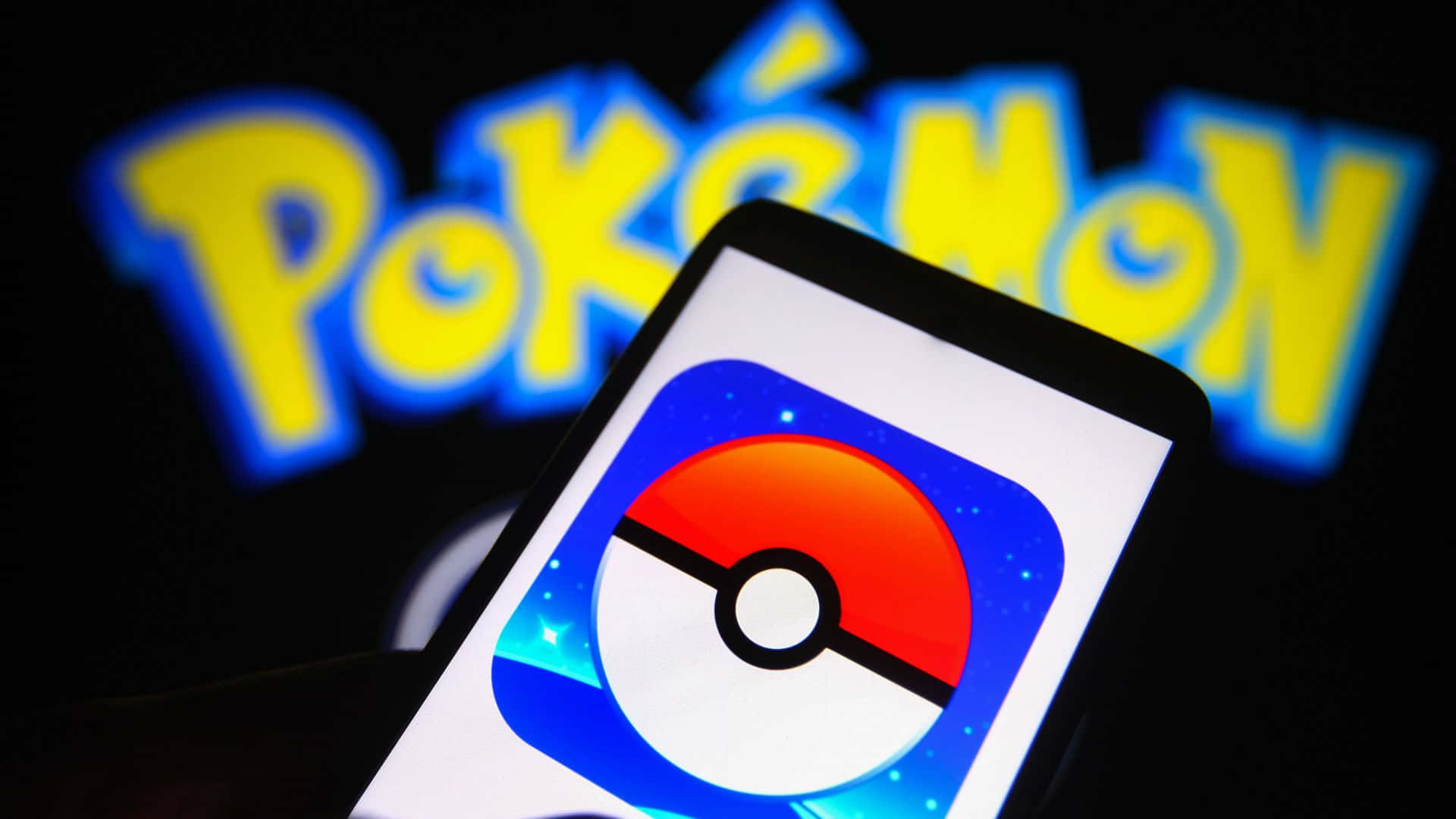 Pokemon Virtual World 桌布 壁紙 — 一部智能手機顯示 Pokémon 應用程式圖標，背景中發光的 Pokémon 標誌模糊不清。