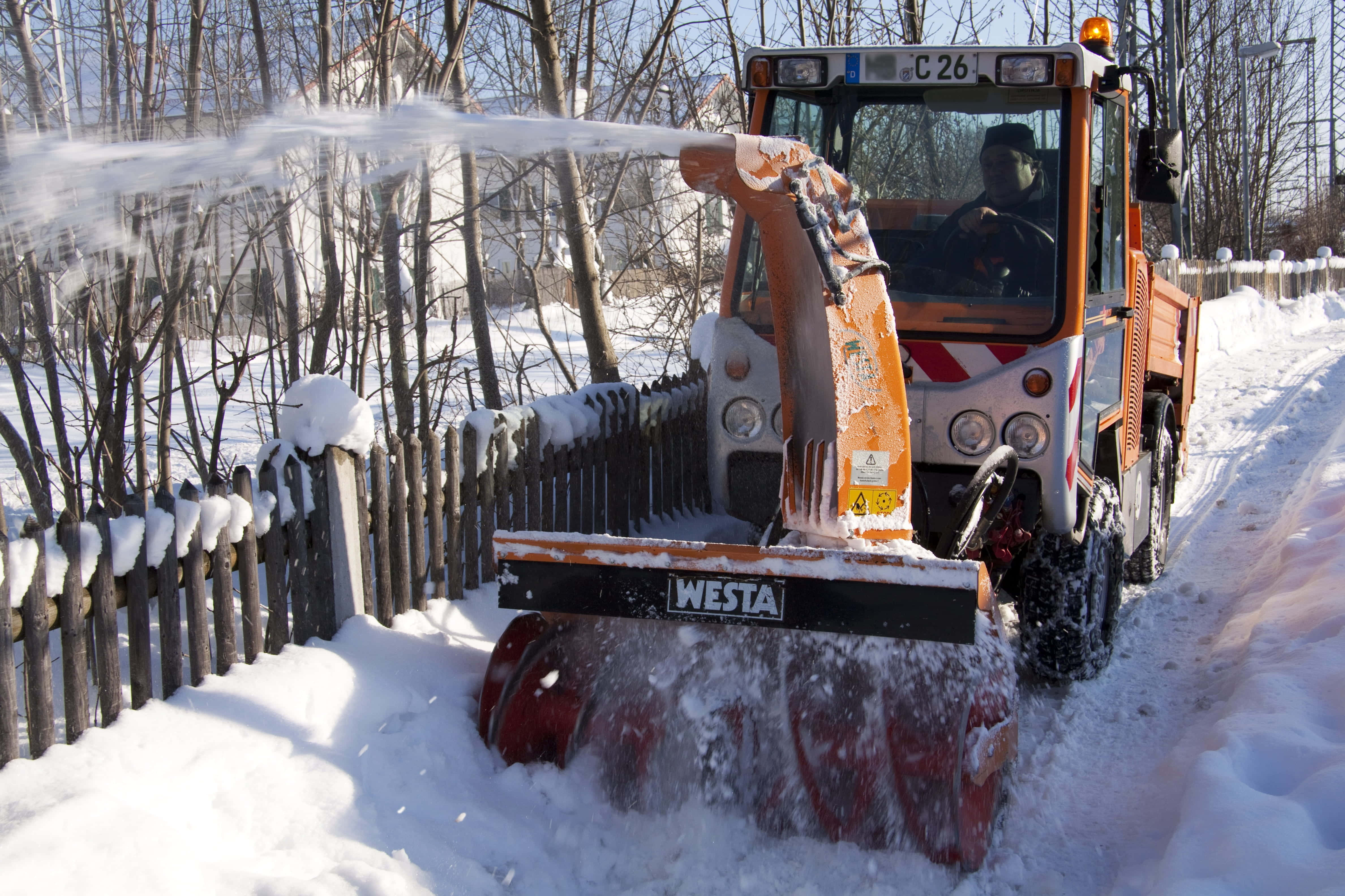 Snowplow 桌布 壁紙 — 一部橙色嘅吹雪機喺明亮嘅冬日陽光下，清理一條被雪覆蓋嘅小路，旁邊係一個沾滿雪嘅木籬笆。