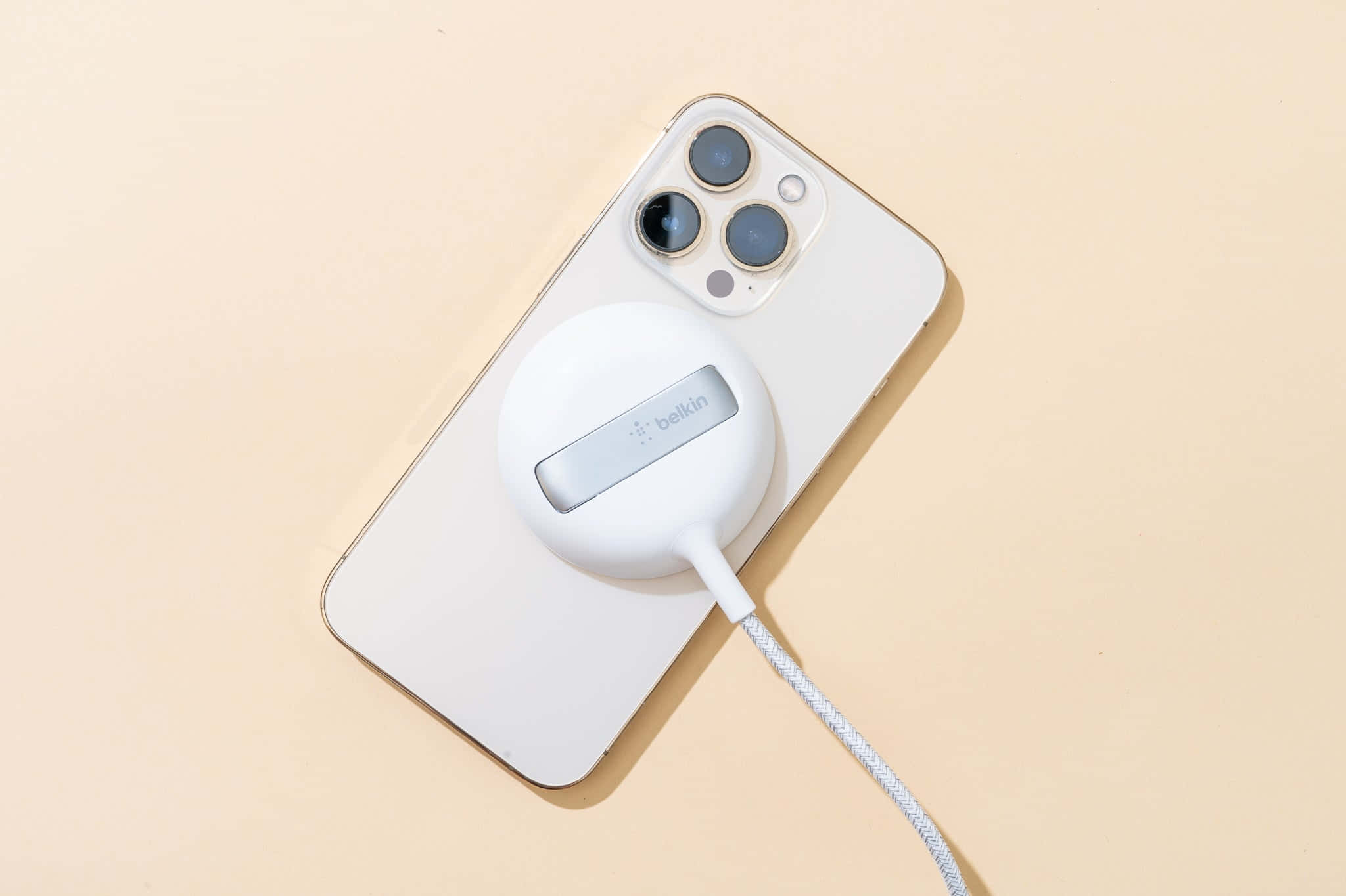 Wireless Charging 桌布 壁紙 — 一部白色iPhone連同磁力充電器放置在柔軟的米色表面上。
