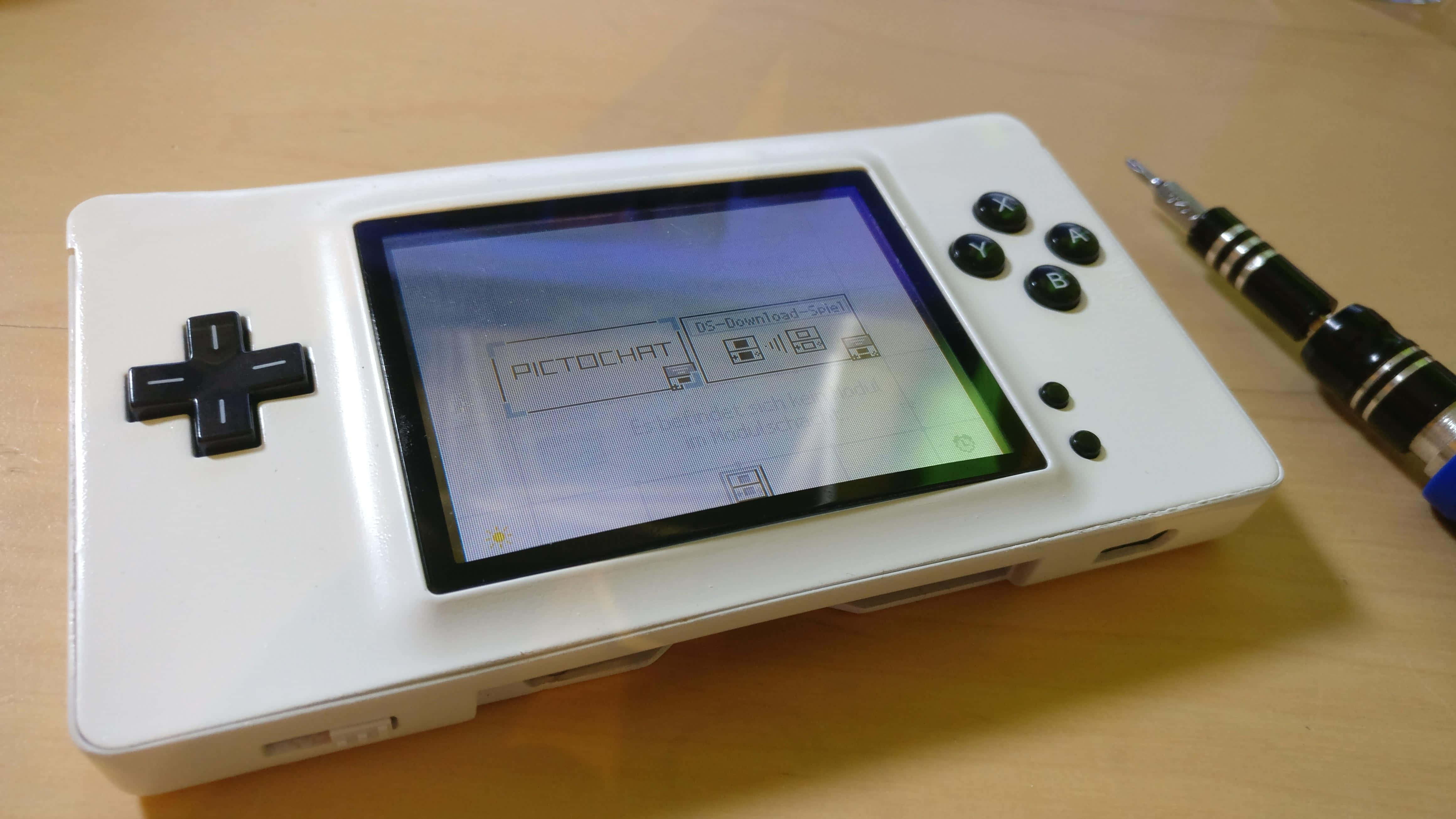 4K Gaming Consoles 桌布 壁紙 — 一部白色手提遊戲機，屏幕上顯示PictoChat，放在木桌上，旁邊有一支觸控筆。