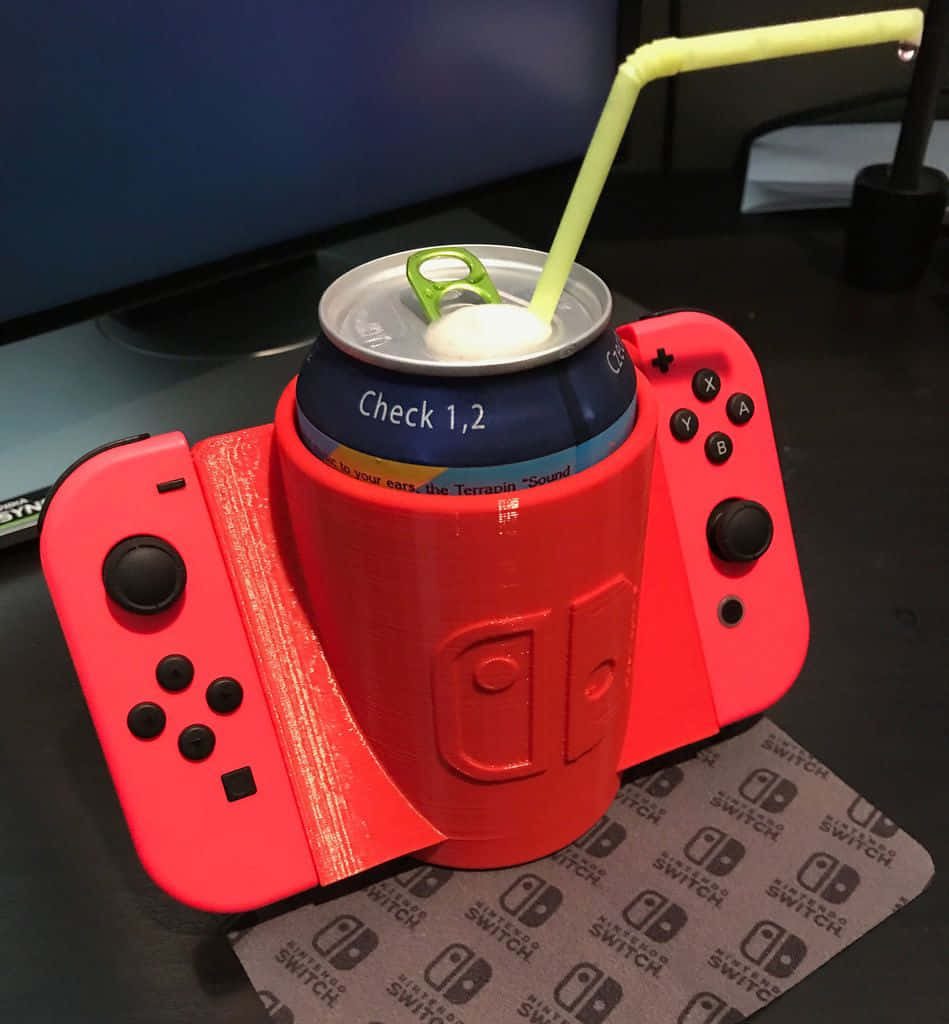 Gaming Accessories 桌布 壁紙 — 一部紅色Nintendo Switch主機被創意地改造成飲料架，用來放置附有吸管的汽水罐。