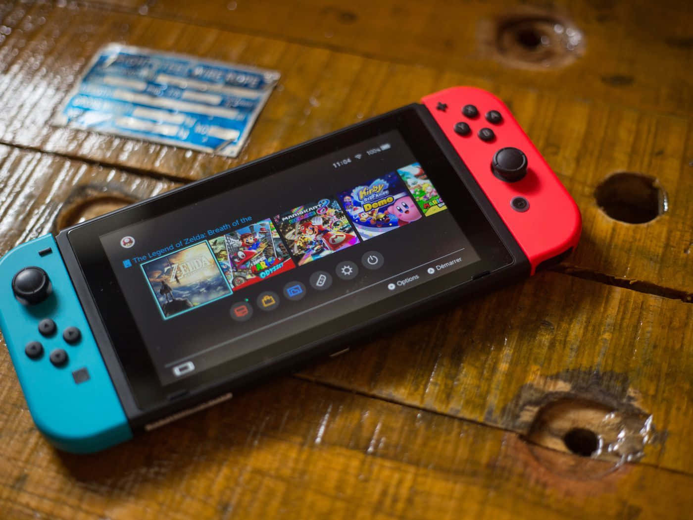 Gaming Consoles 桌布 壁紙 — 一部紅藍色Nintendo Switch放在風化的木桌上，顯示色彩繽紛的遊戲圖標。