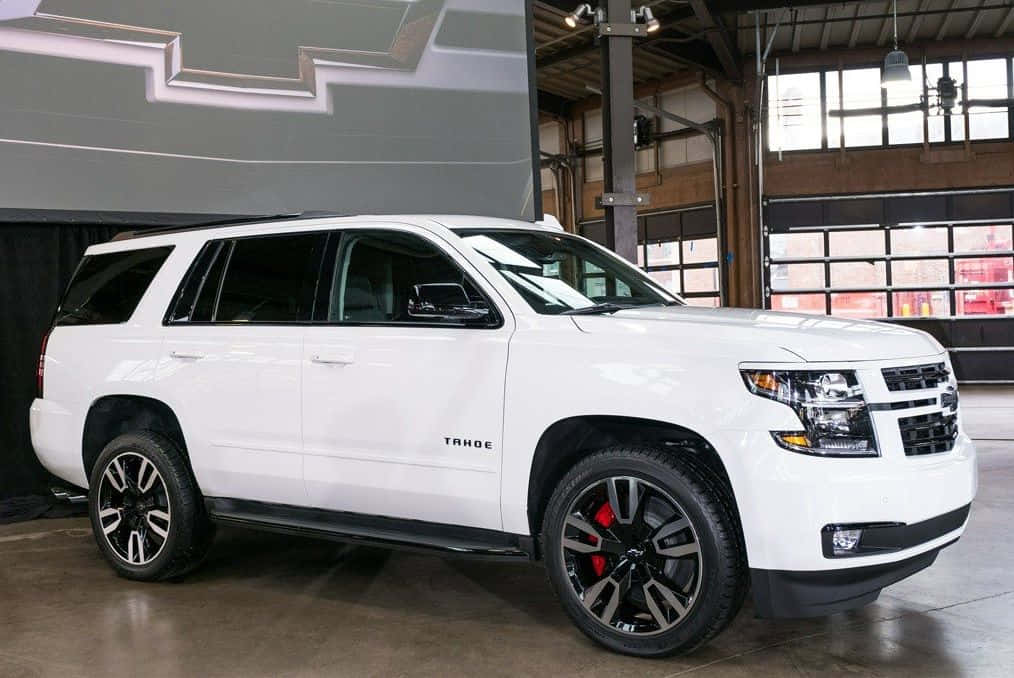 Family Car 桌布 壁紙 — 一部純白色雪佛蘭Tahoe SUV，配備黑色輪圈和紅色制動卡鉗，在一個高天花板、大窗戶的現代工業車庫中展示。