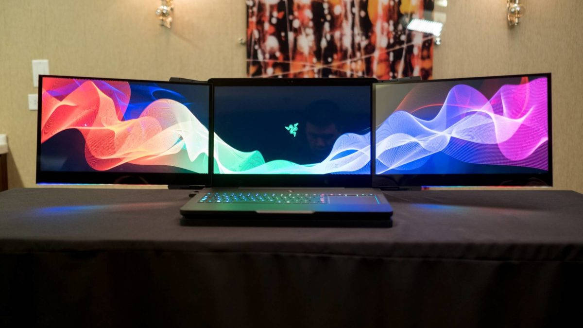 4K 桌布 壁紙 — 一部纖薄手提電腦放在深色桌子中央，兩側有兩部曲面顯示器顯示充滿活力的抽象波浪桌布。