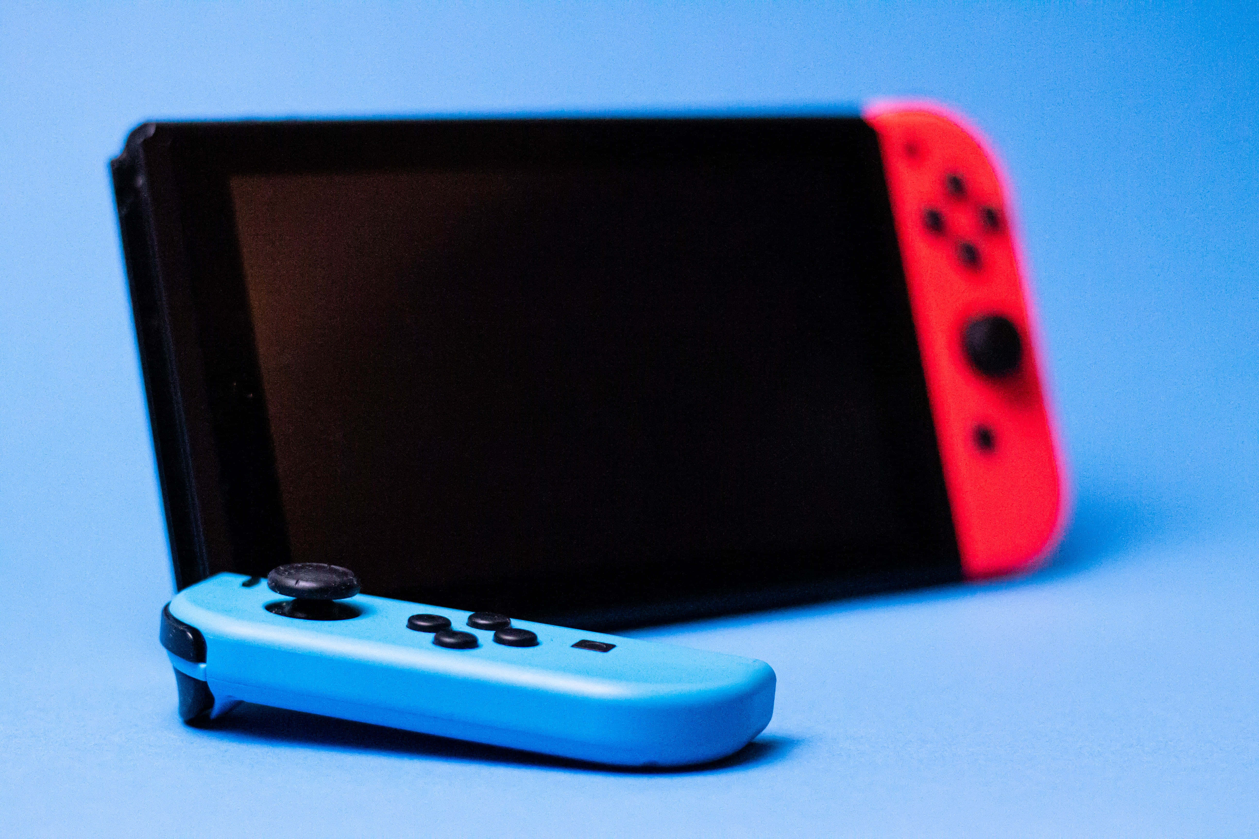 Gaming Consoles 桌布 壁紙 — 一部藍色和紅色的Nintendo Switch主機，帶有分離式控制器，放置在純藍色背景上。