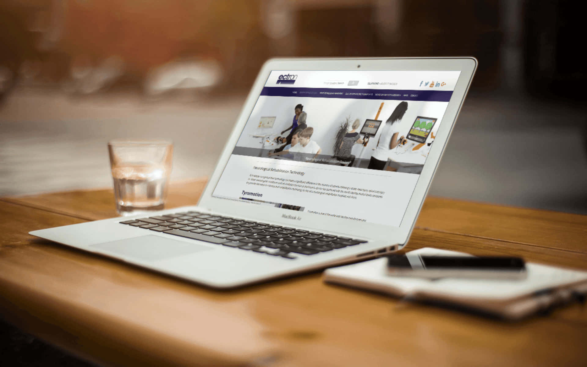 Website 桌布 壁紙 — 一部銀色手提電腦在木桌上顯示醫療網站，旁邊有一杯水和記事簿。