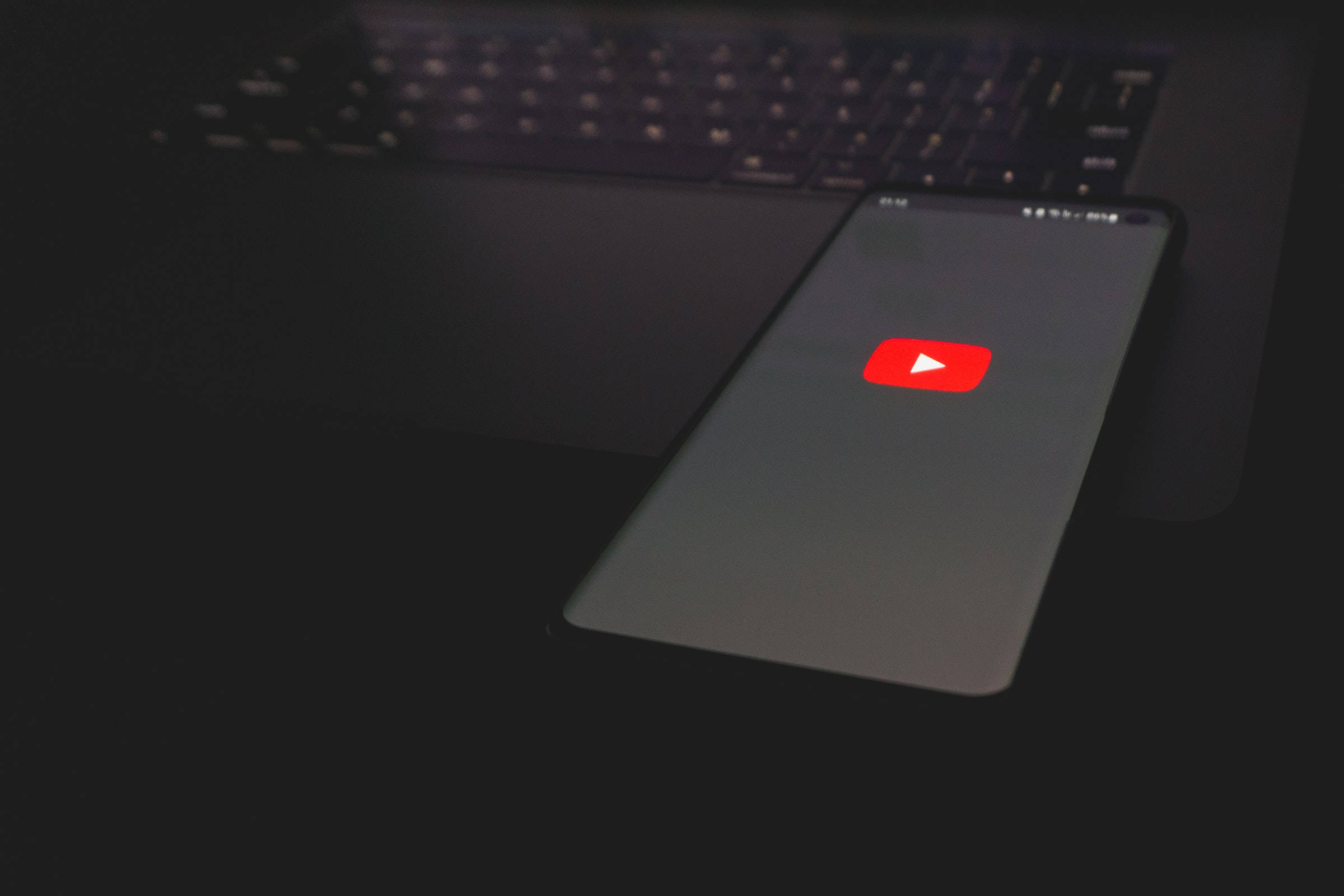 Application 桌布 壁紙 — 一部顯示 YouTube 標誌的智能手機放在昏暗環境中的深色筆記型電腦鍵盤上。