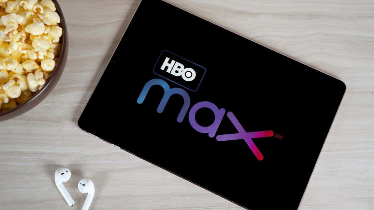 Video-on-demand 桌布 壁紙 — 一部顯示HBO Max標誌的平板電腦，旁邊放著一碗爆谷和白色耳塞，置於淺色木質表面上。