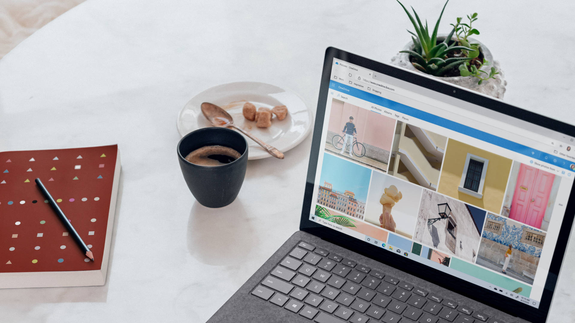 Working From Home 桌布 壁紙 — 一部顯示彩色庫存照片的筆記型電腦放在白色大理石桌上，旁邊有咖啡杯、筆記本和盆栽多肉植物。