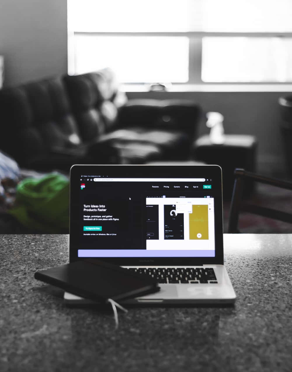 Website 桌布 壁紙 — 一部顯示設計軟件網站的筆記型電腦放在花崗岩枱面上，背景是單色調的客廳和梳化。