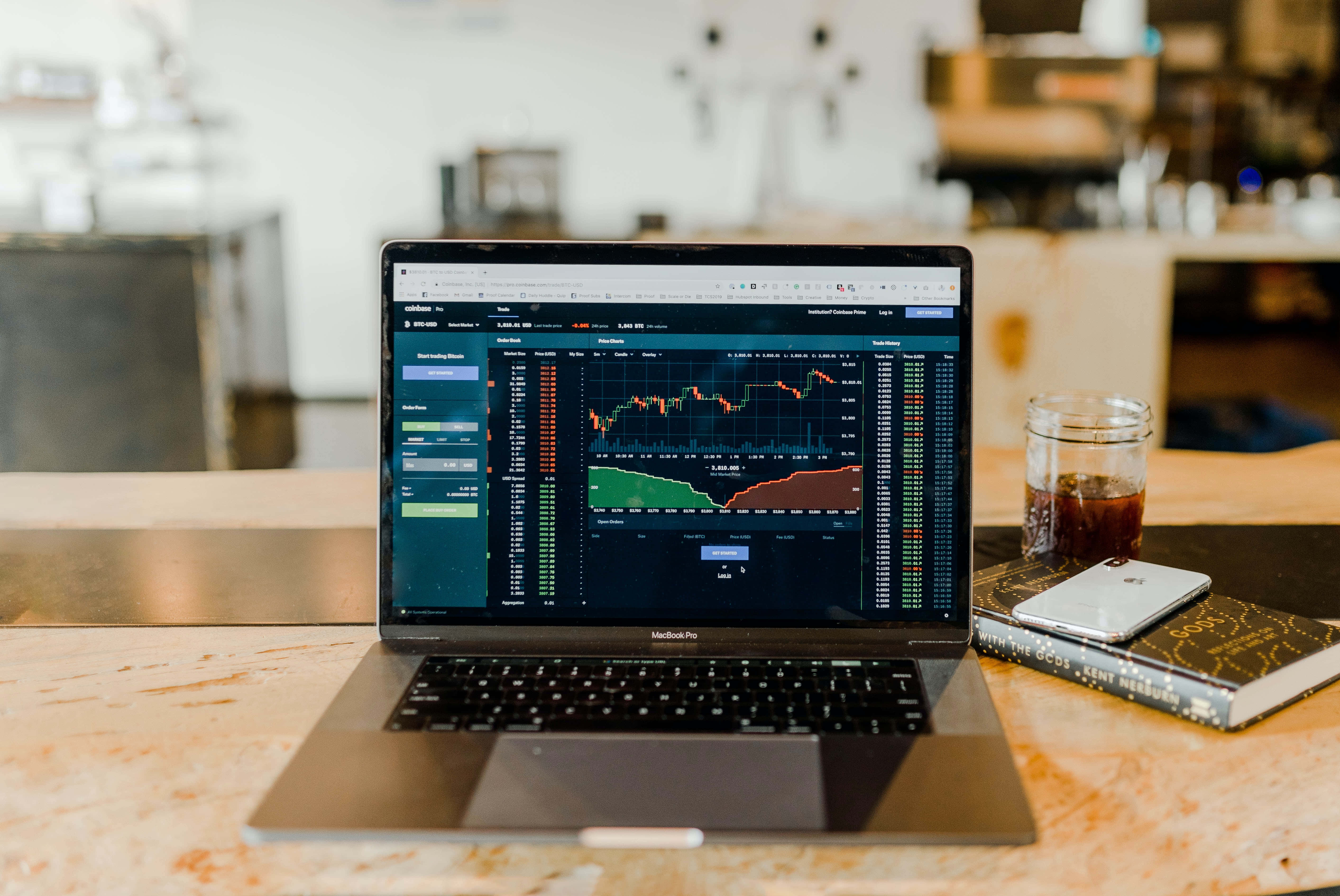 Trading 桌布 壁紙 — 一部顯示財務圖表的筆記型電腦放在現代咖啡館的大理石檯面上，旁邊有一杯咖啡和一本書。