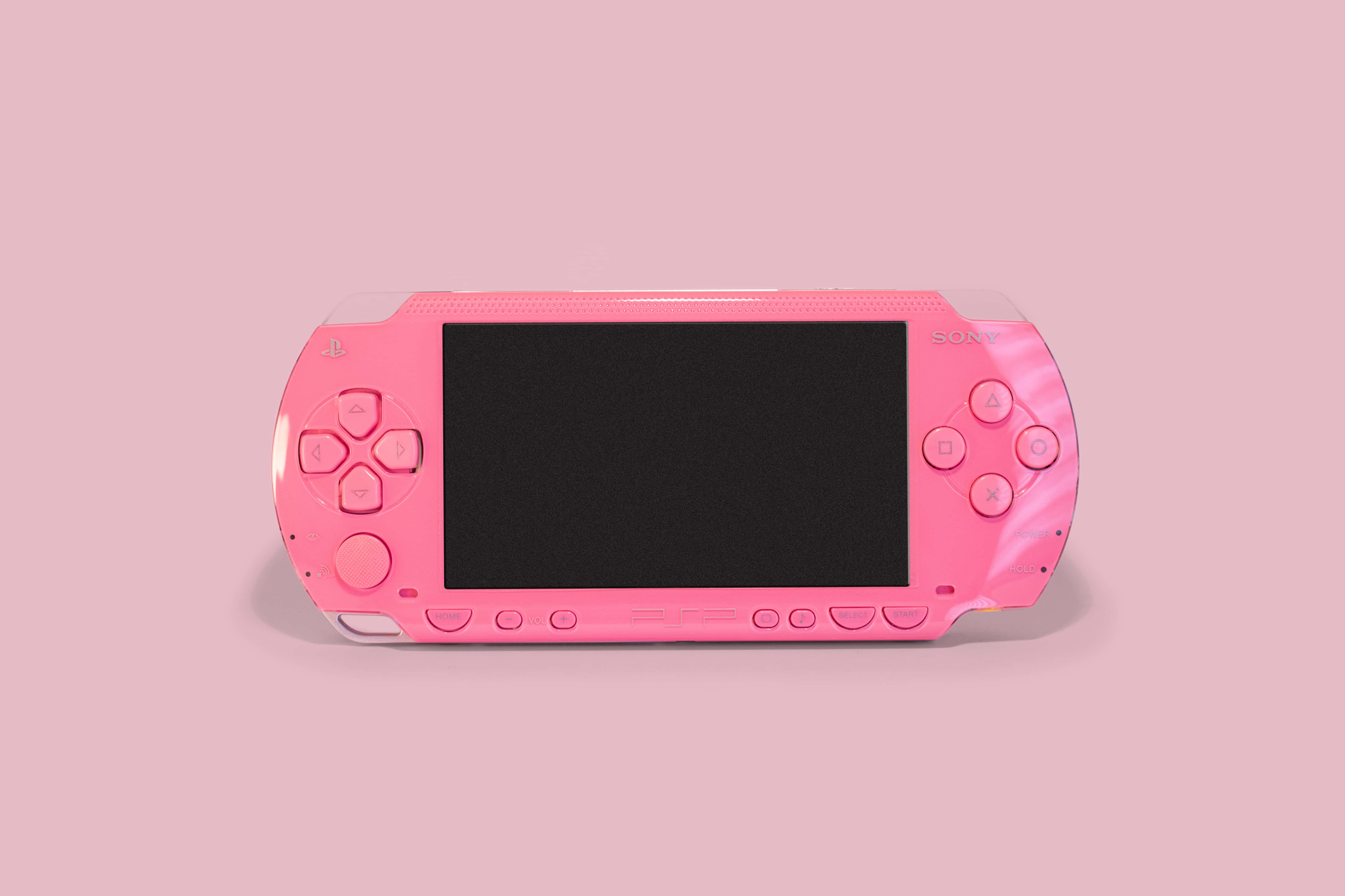 Gaming Consoles 桌布 壁紙 — 一部鮮粉紅色的 Sony PlayStation Portable 主機，置於柔和粉紅背景中央，配以乾淨的影樓燈光。