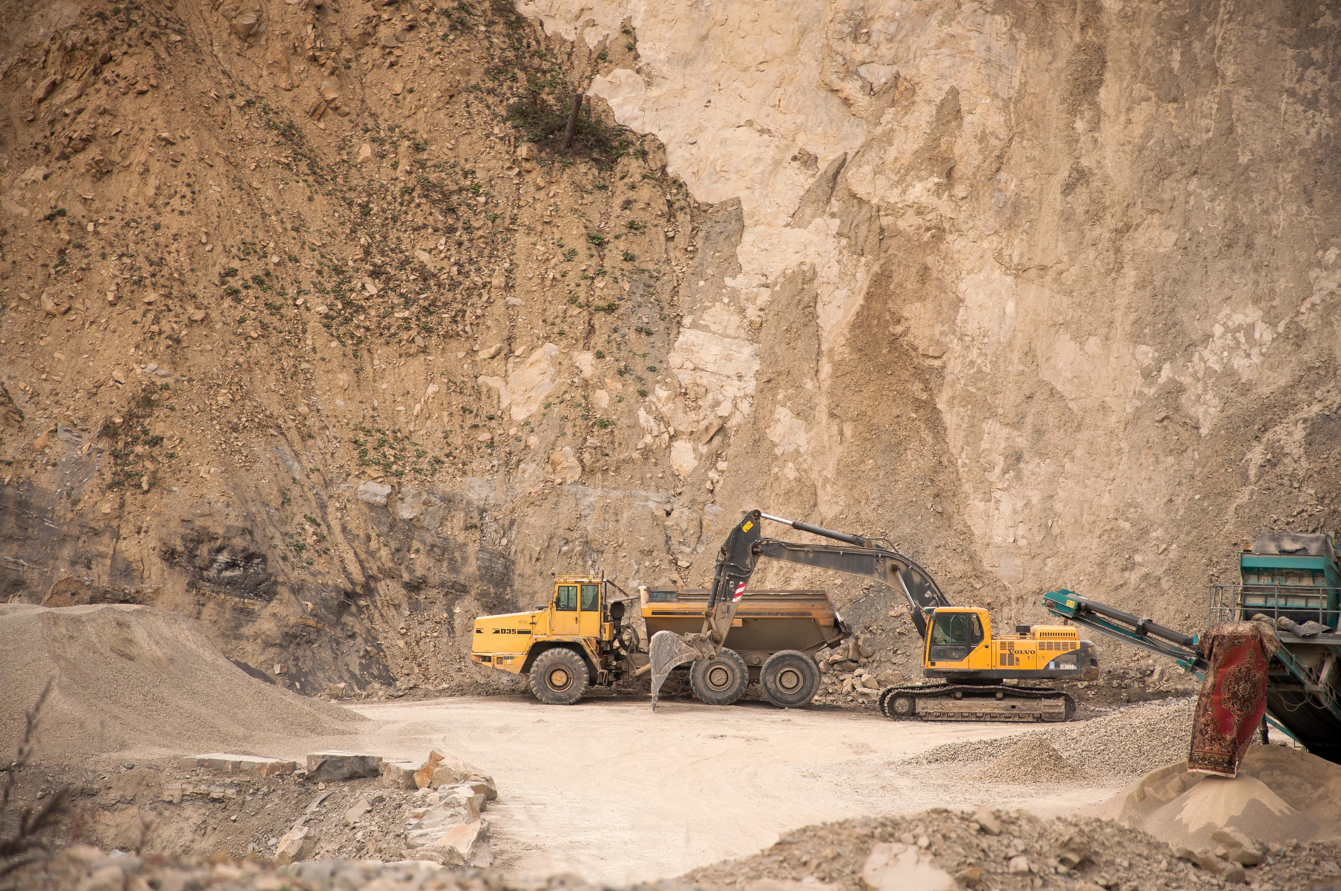 Mining 桌布 壁紙 — 一部黃色挖掘機喺崎嶇嘅採石場，喺高聳嘅岩壁之間，將礫石裝載到傾卸車上。