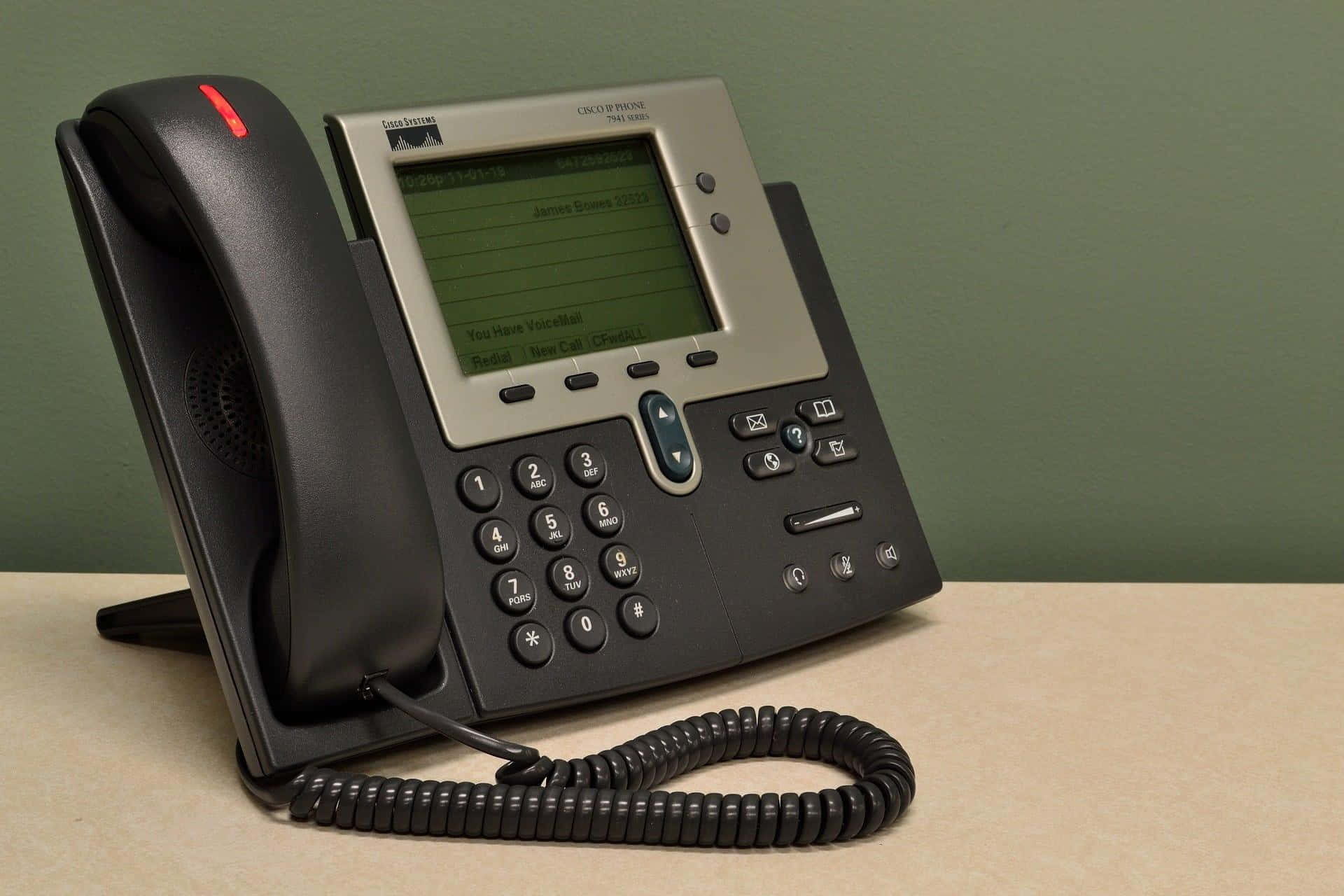 Telemarketing 桌布 壁紙 — 一部黑色Cisco辦公室電話連螺旋電線放在米色桌上，背景係柔和嘅綠色牆。
