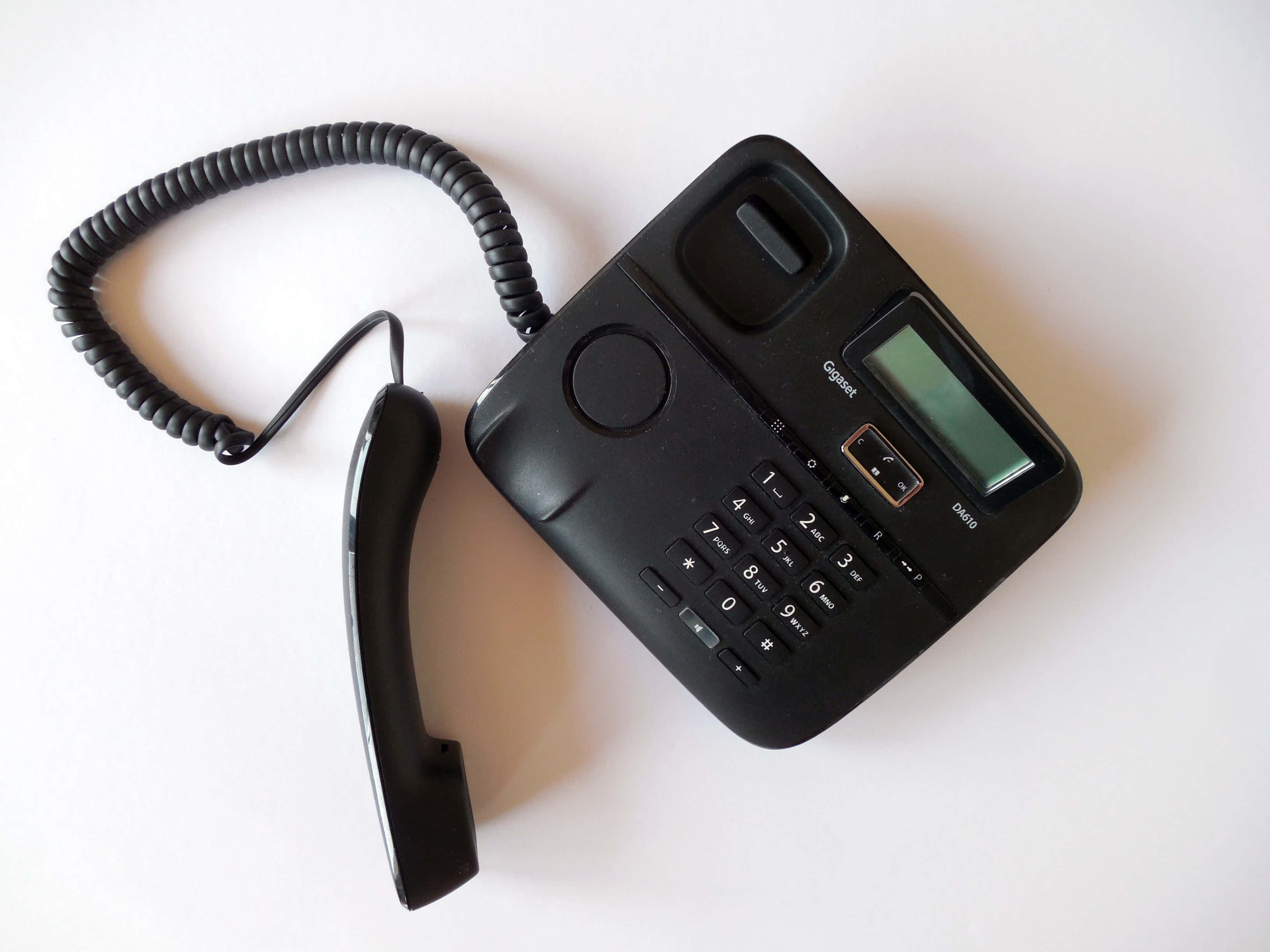 Phone Call 桌布 壁紙 — 一部黑色有線電話連聽筒放置在純白色表面上，展示其鍵盤和小屏幕。