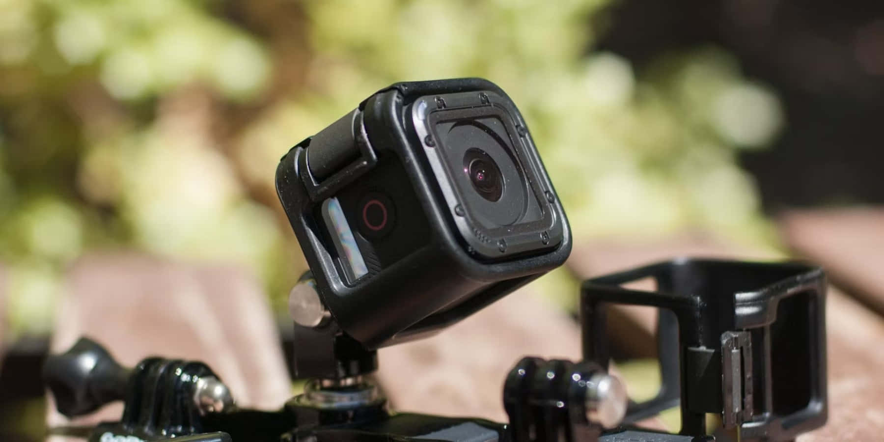 gopro 桌布 壁紙 — 一部黑色運動相機安裝在三腳架上，背景有模糊的綠色樹葉。