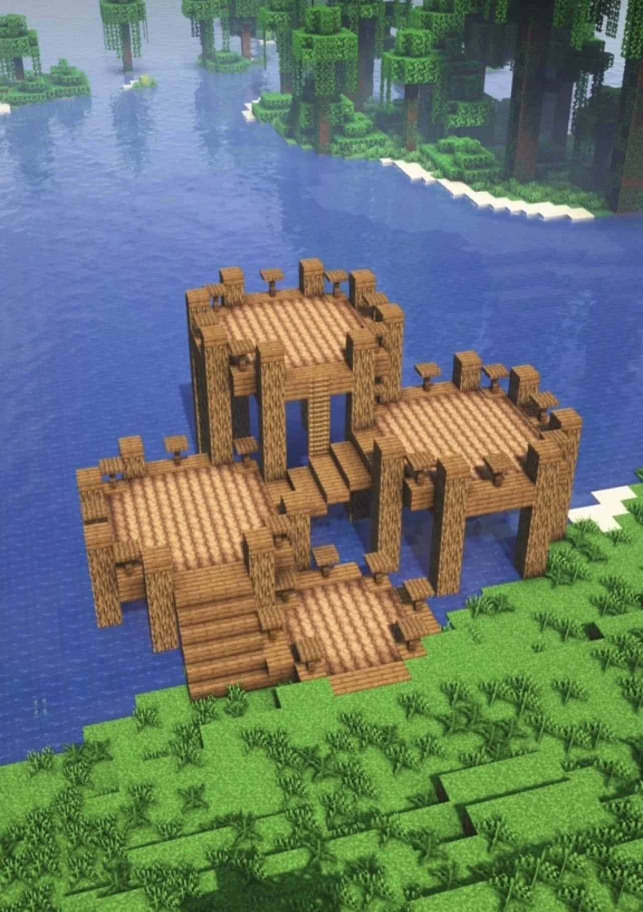 Minecraft Architecture 桌布 壁紙 — 一間像素化的木屋，有多層和樓梯，坐落於草地岸邊，旁邊是一個平靜的藍色湖泊，周圍是森林覆蓋的島嶼。