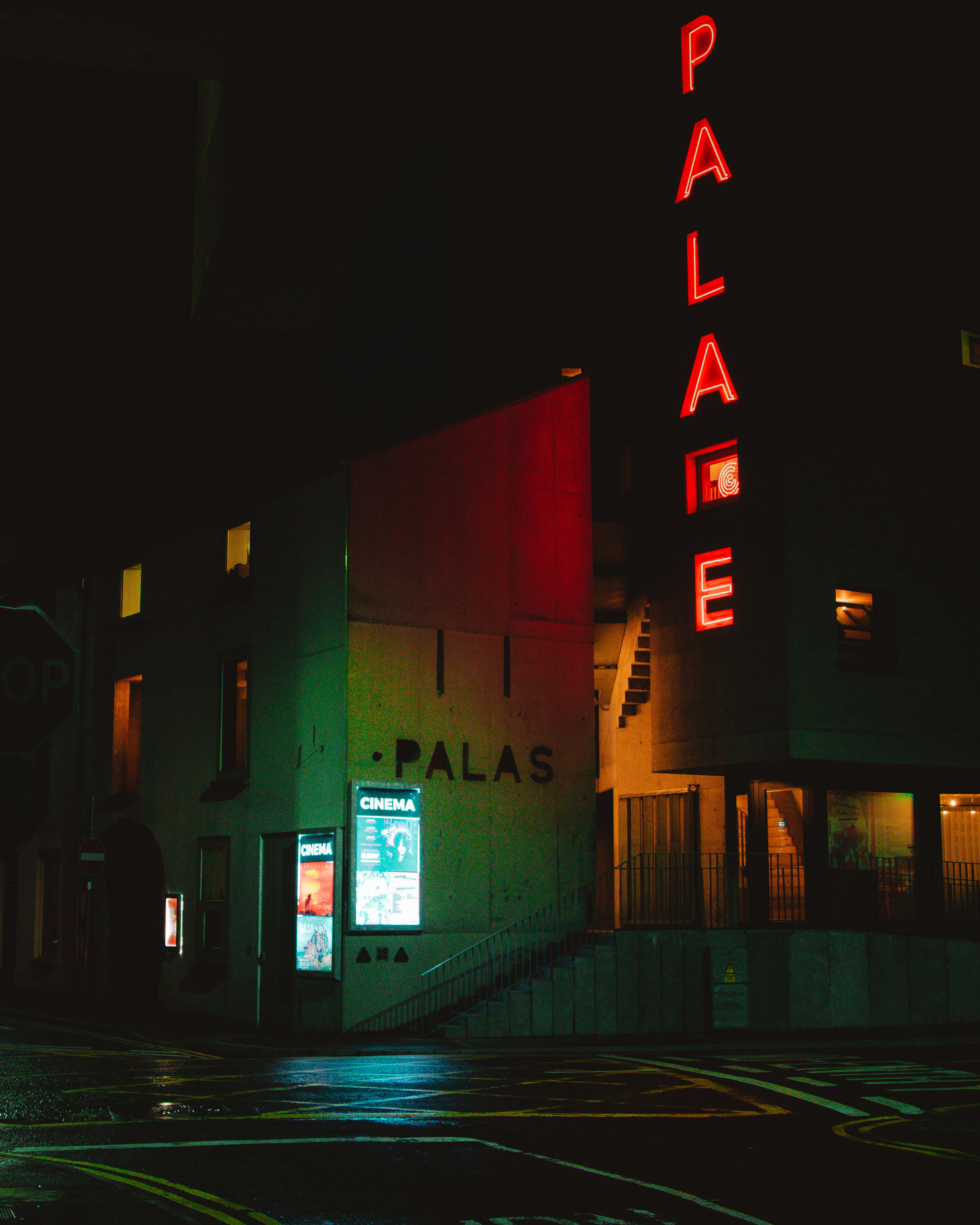 Vibes 桌布 壁紙 — 一間名為「PALACE」的霓虹燈電影院，在漆黑的都市夜晚中發出紅光，濕漉漉的人行道反射出五彩繽紛的燈光。
