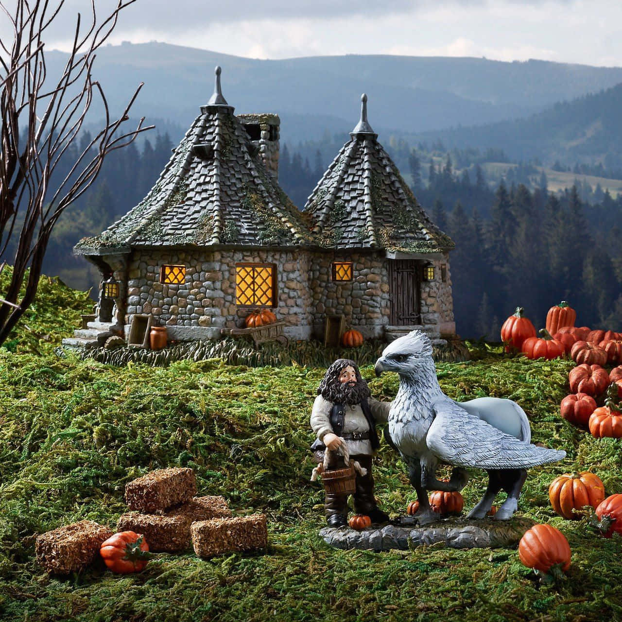 Hagrid's Hut 桌布 壁紙 — 一間夢幻的石頭小屋，窗戶閃爍著光芒，坐落在長滿青苔的山坡上，周圍環繞著南瓜和一個巨大的鳥雕像。