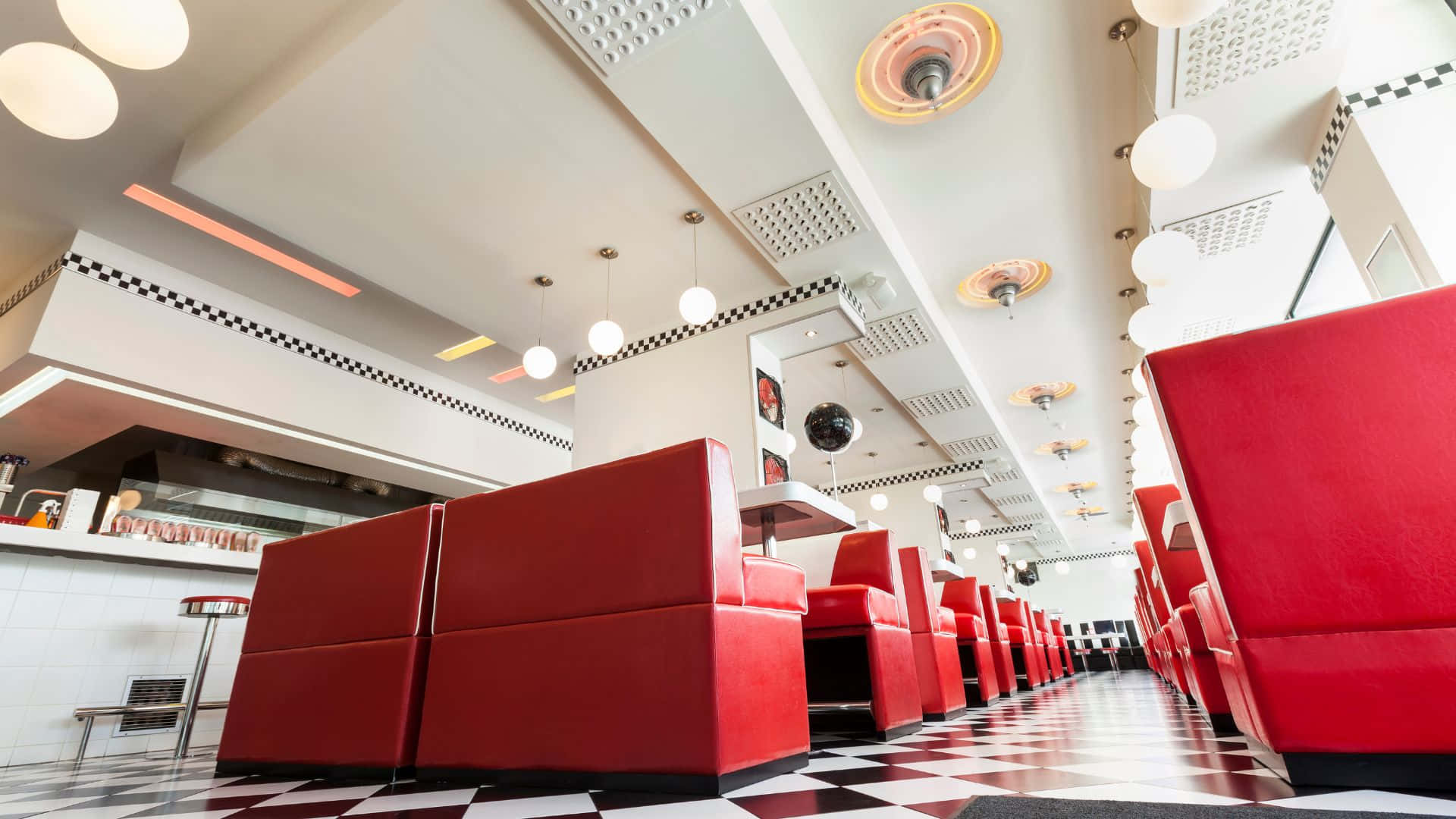 Diner 桌布 壁紙 — 一間復古風格的餐廳，設有鮮紅色卡座和黑白棋盤格地板，上方是明亮的吊燈。