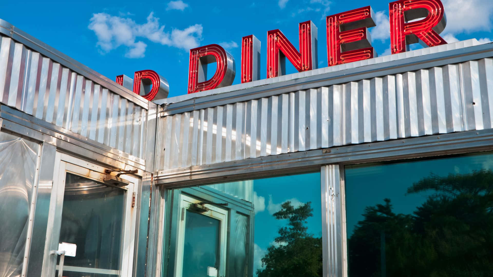 Diner 桌布 壁紙 — 一間復古餐廳，在藍天白雲下有一個明亮的紅色霓虹燈招牌。