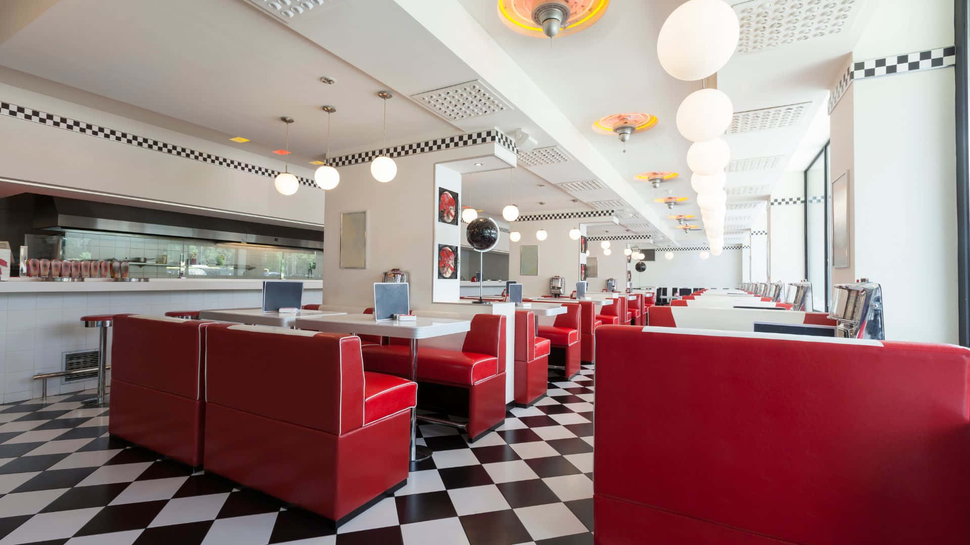 Diner 桌布 壁紙 — 一間復古餐廳，設有紅色卡座和黑白棋盤地板，上方懸掛著明亮的吊燈。