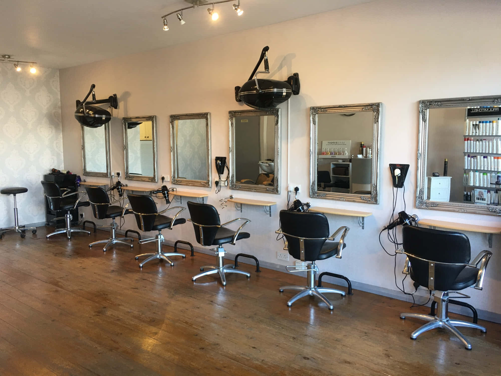 Hair Salon 桌布 壁紙 — 一間明亮現代的美髮沙龍，配有黑色造型椅、銀色鏡子和木地板，在溫暖的頭頂燈光下。