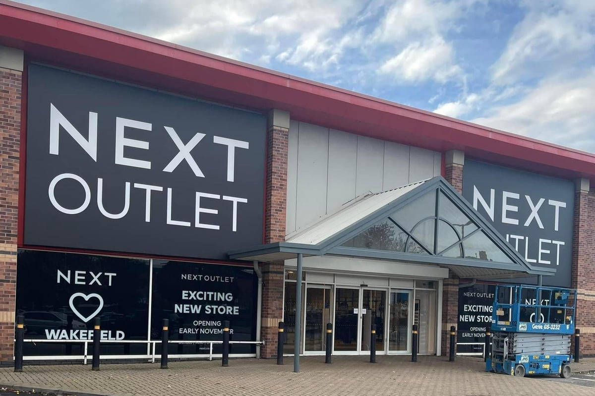 Next Outlet 壁紙 — 一間現代磚牆和玻璃的Next Outlet商店，在部分多雲的天空下設有大膽的招牌。