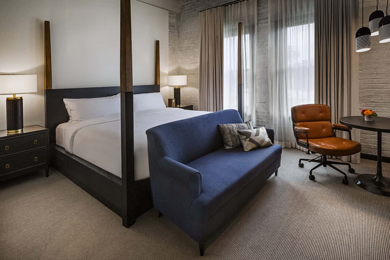 Hotel Room 桌布 壁紙 — 一間現代酒店客房，配備四柱床、藍色梳化、皮革椅子和讓自然光透入的大窗戶。