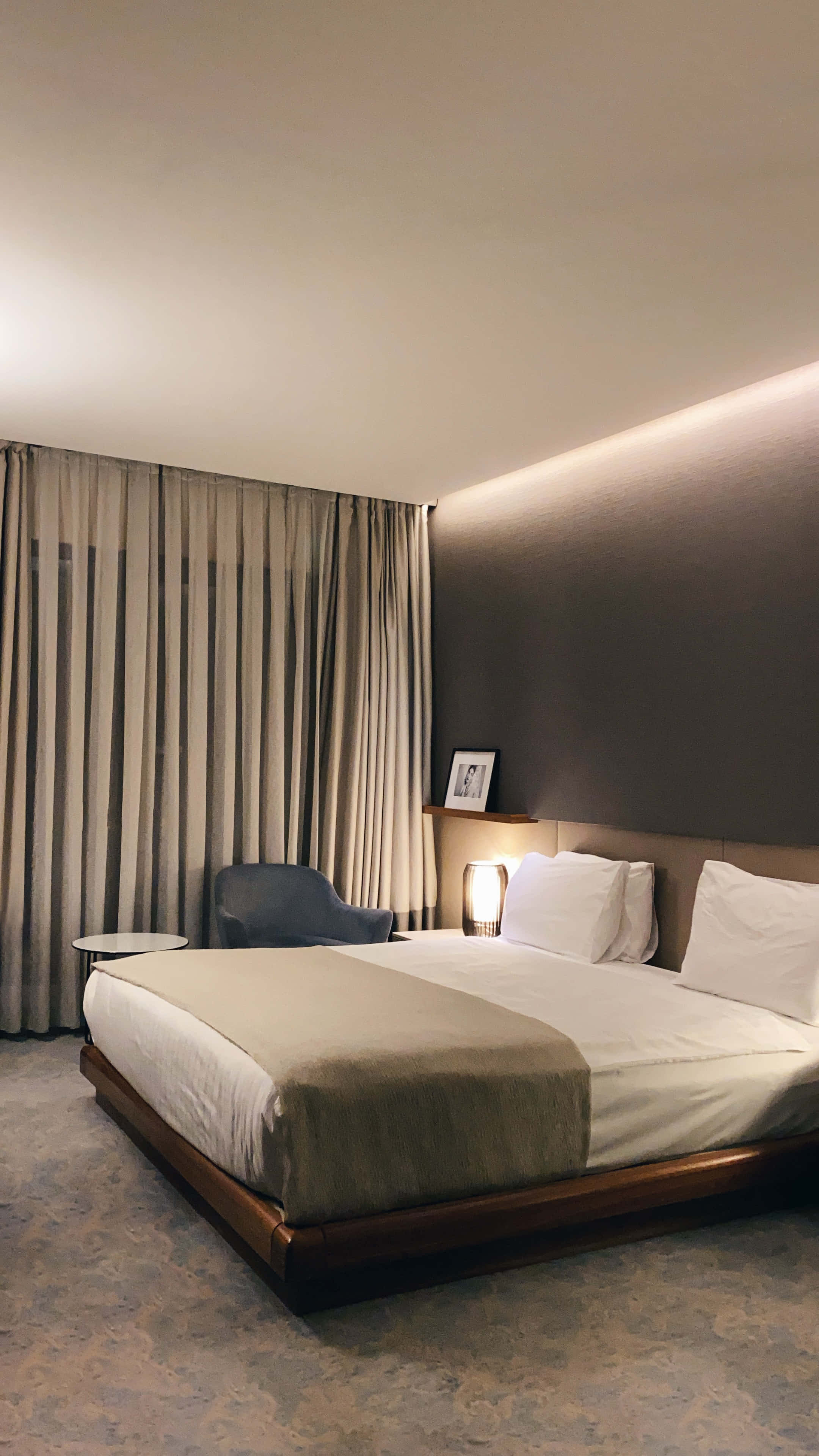 Hotel Room 桌布 壁紙 — 一間現代酒店客房，配有一張整齊鋪好的床，在溫暖的環境燈光和落地窗簾下。