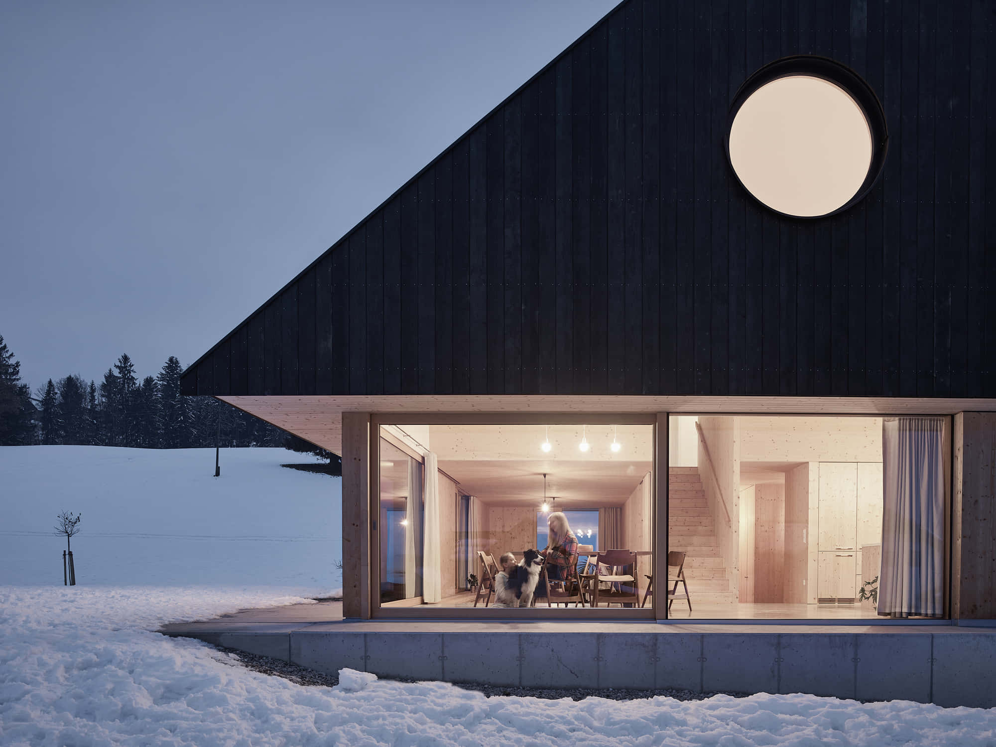 Minimalist Architecture 桌布 壁紙 — 一間現代黑色木屋，帶有圓形窗戶，在雪景暮色中溫暖地發光。