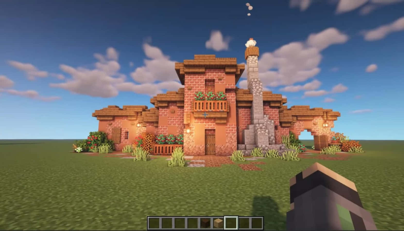 Cool Minecraft 桌布 壁紙 — 一間舒適的像素風Minecraft房屋，帶有石頭煙囪和花箱，矗立在藍天白雲下的草地上。