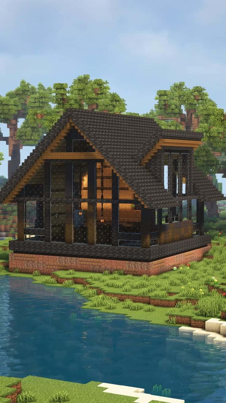 Minecraft Architecture 桌布 壁紙 — 一間舒適的像素風小屋，有木樑和玻璃牆，坐落在平靜的藍色湖泊旁，周圍是塊狀的綠色樹木，天空晴朗。