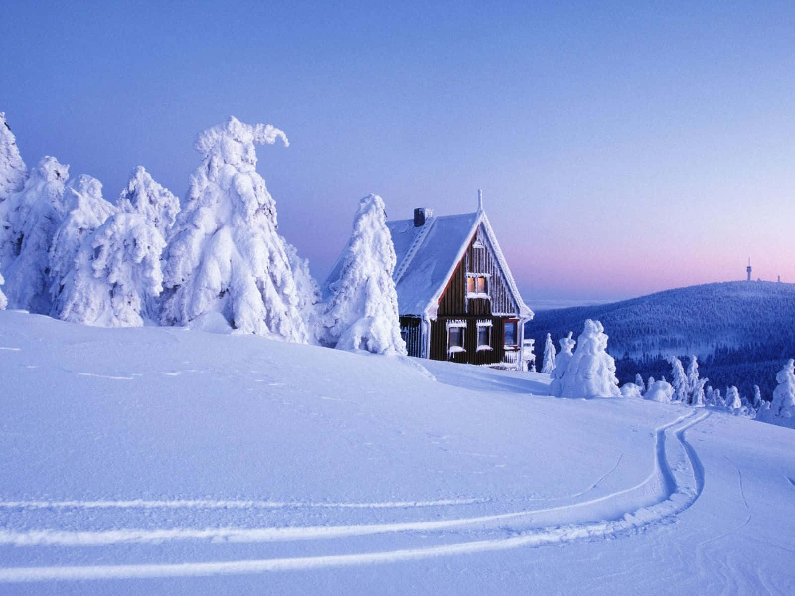 Winter Scene 桌布 壁紙 — 一間舒適的木屋坐落在暮色中白雪覆蓋的山景中，周圍是結霜的樹木，滑雪道蜿蜒穿過純淨的白雪。