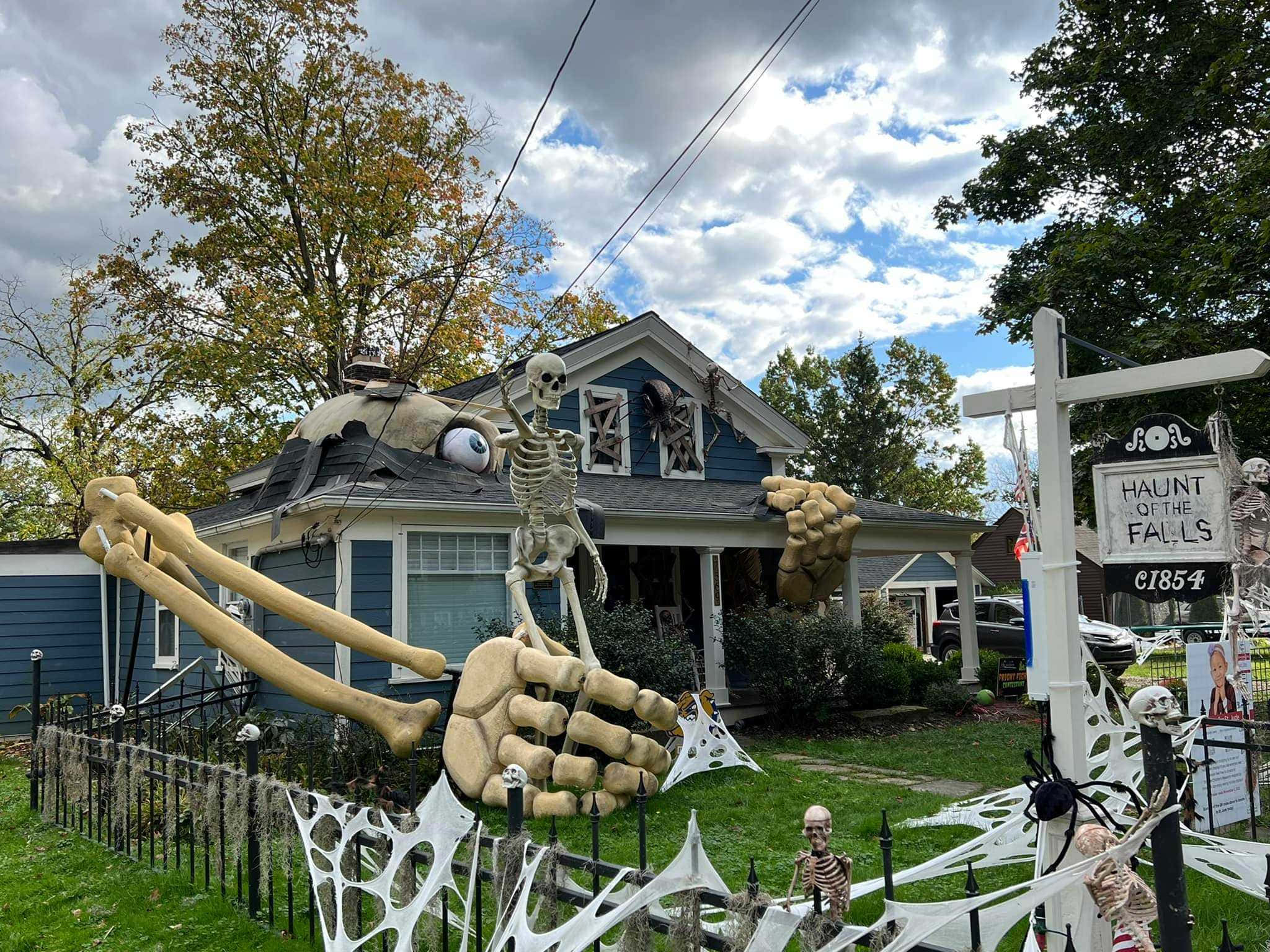 Halloween Yard Decorations 桌布 壁紙 — 一間藍色房屋，在陰天之下為萬聖節裝飾了巨型骷髏道具和蜘蛛網。