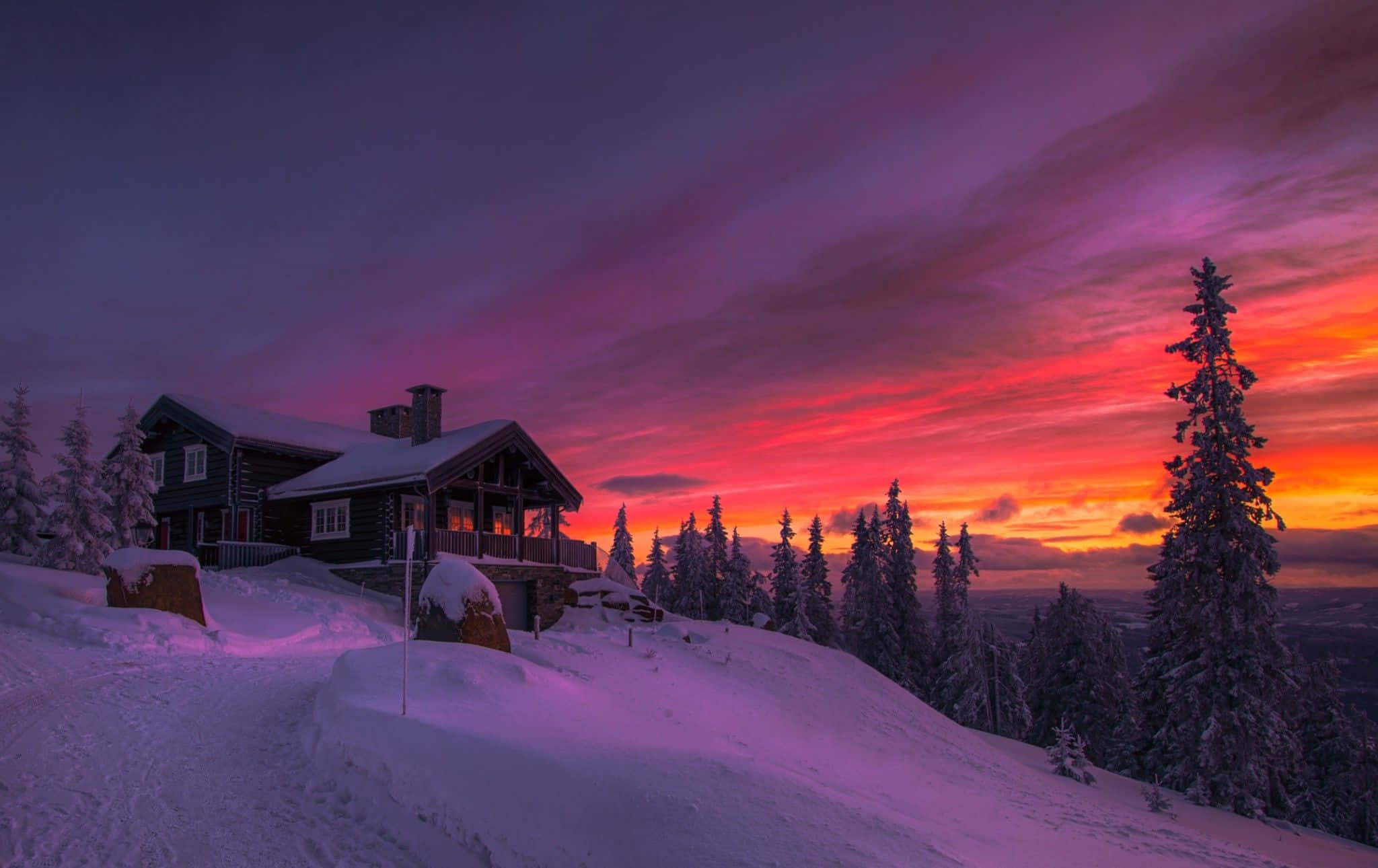 Winter Sunset 桌布 壁紙 — 一間被雪覆蓋的小屋在充滿活力的紫色和橙色冬季日落天空下溫暖地發光。